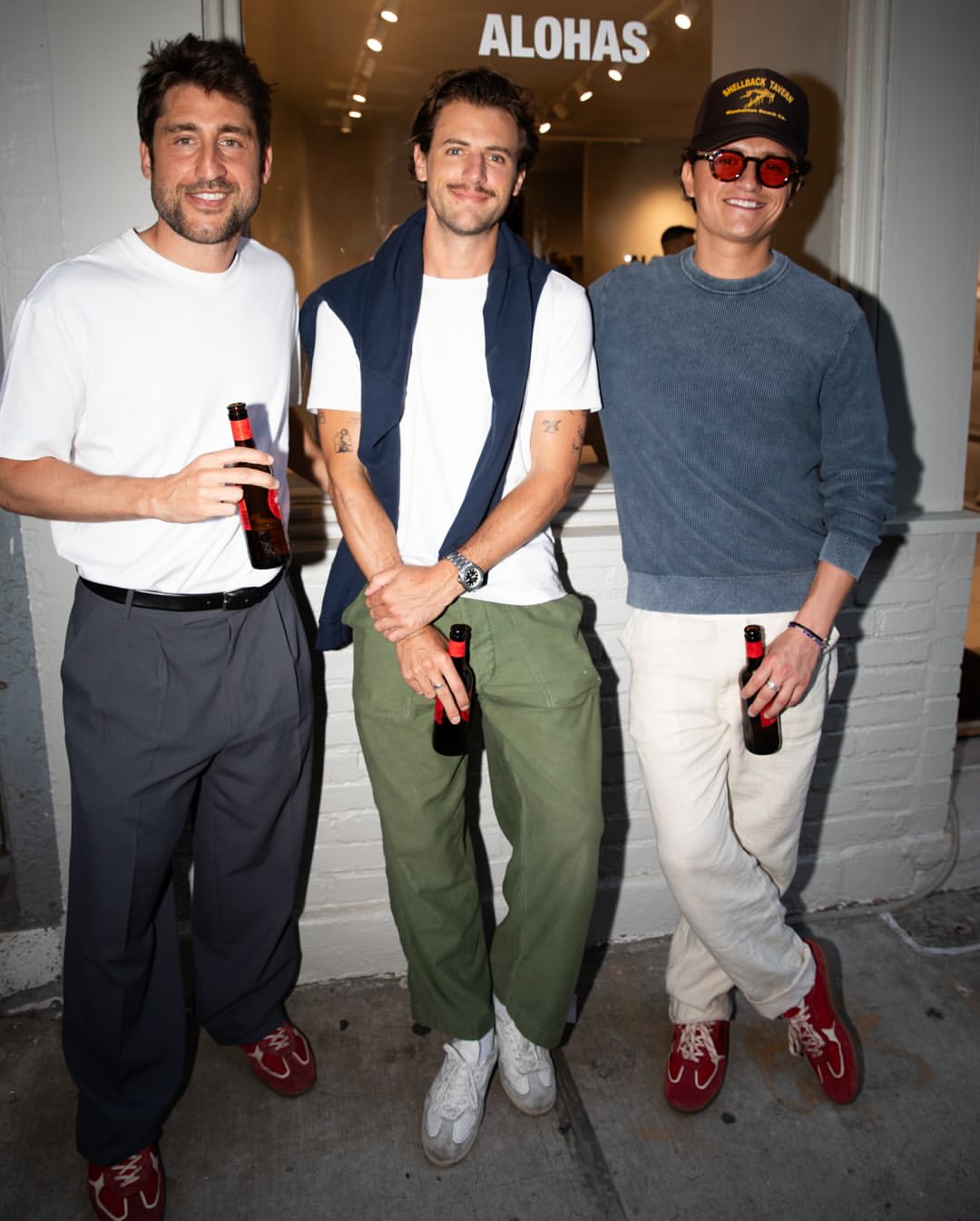 Guests stand outside the Alohas New York retail store during opening night, holding drinks with the illuminated interior and logo signage visible behind them.