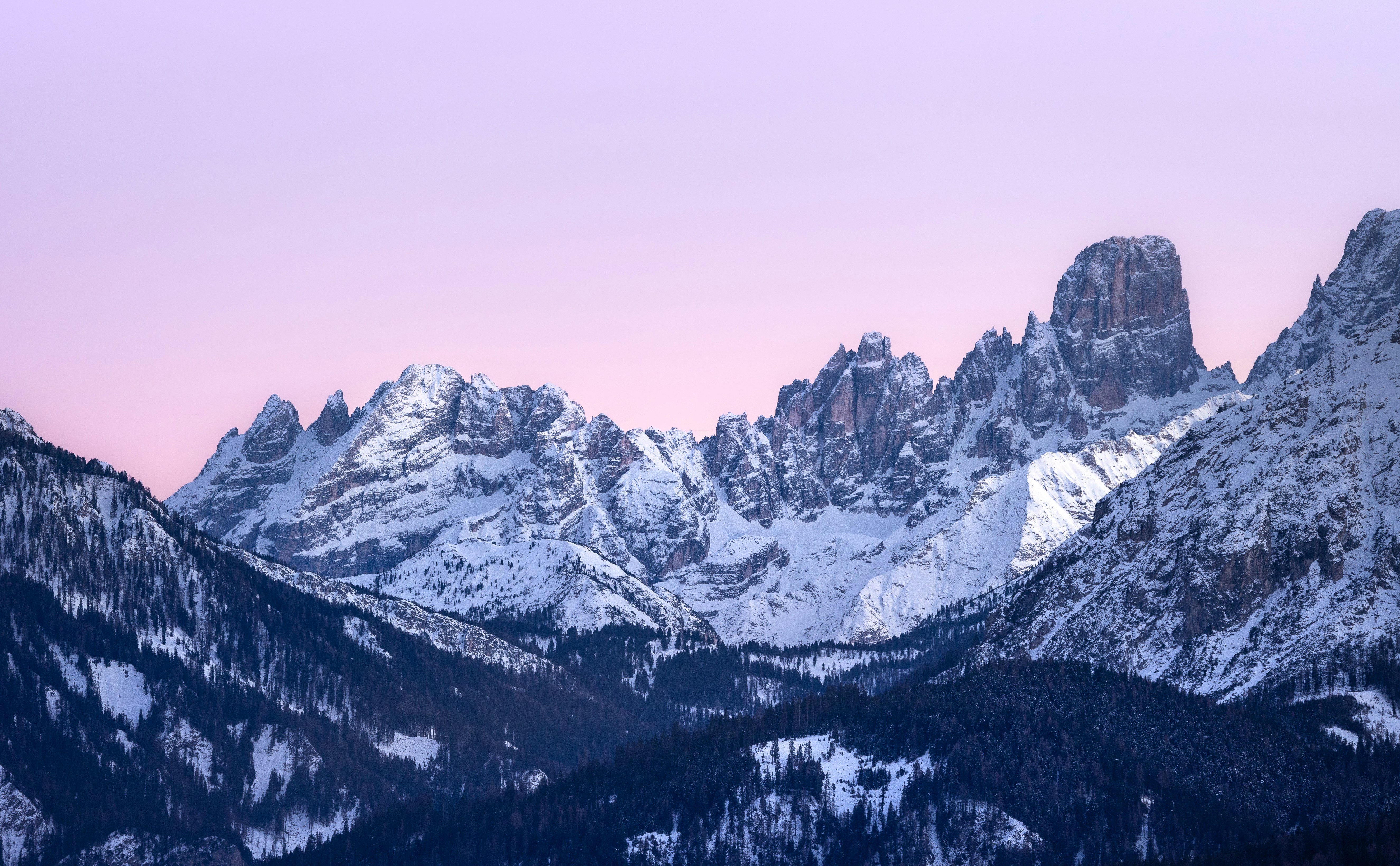 Snow-covered mountains under a soft pink sky