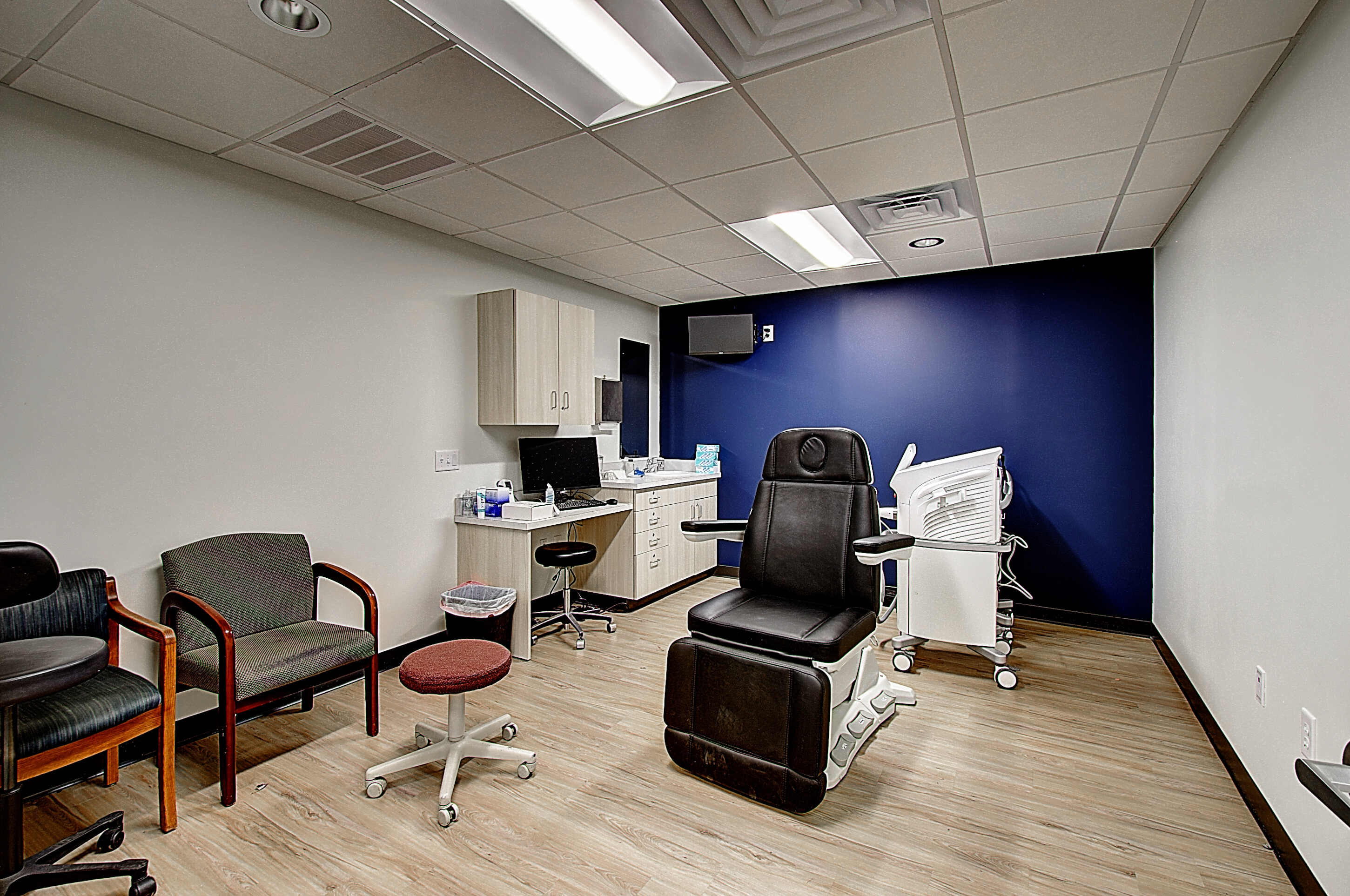 An empty office space featuring an exam chair, computer, and seating arranged around the room.
