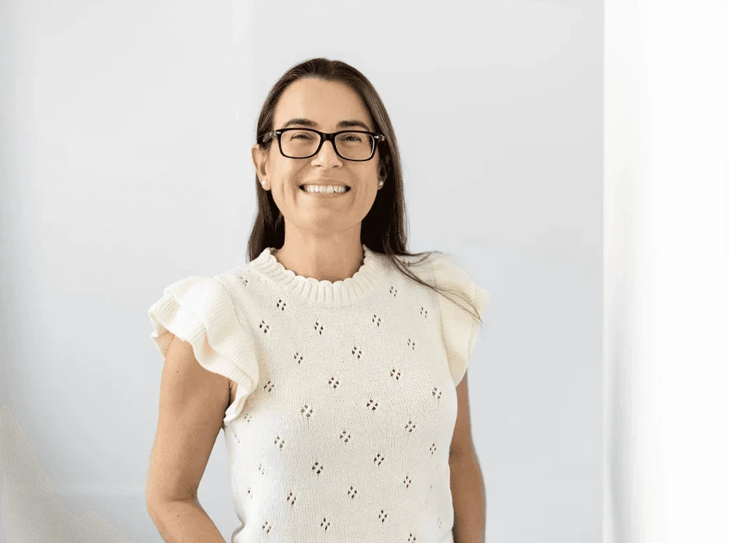 Smiling woman with dark hair and glasses, wearing a cream knitted top, representing one of the key investors.