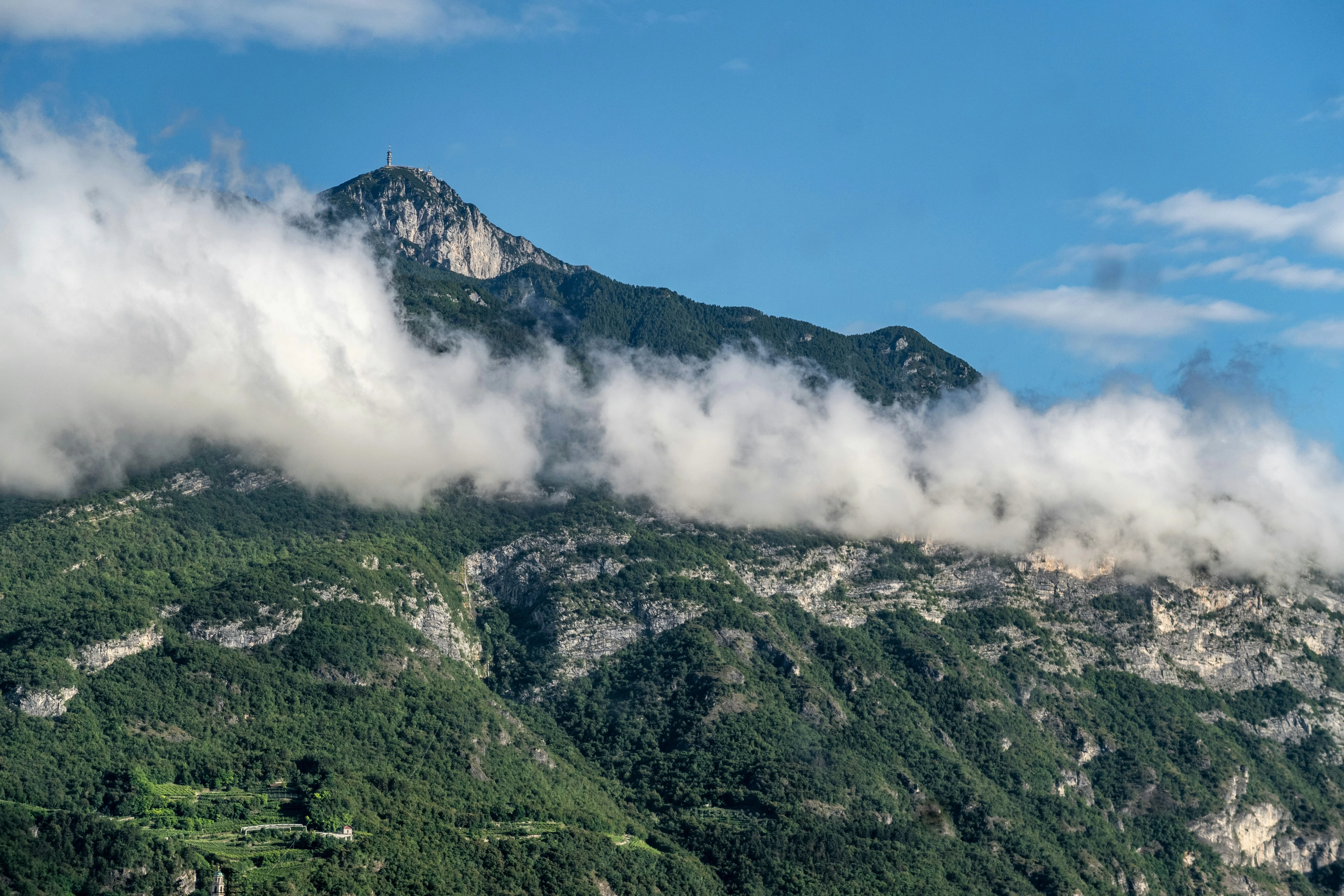 Lush green Italian mountain peak partially obscured by a dramatic layer of clouds, emphasizing the altitude and source of water.