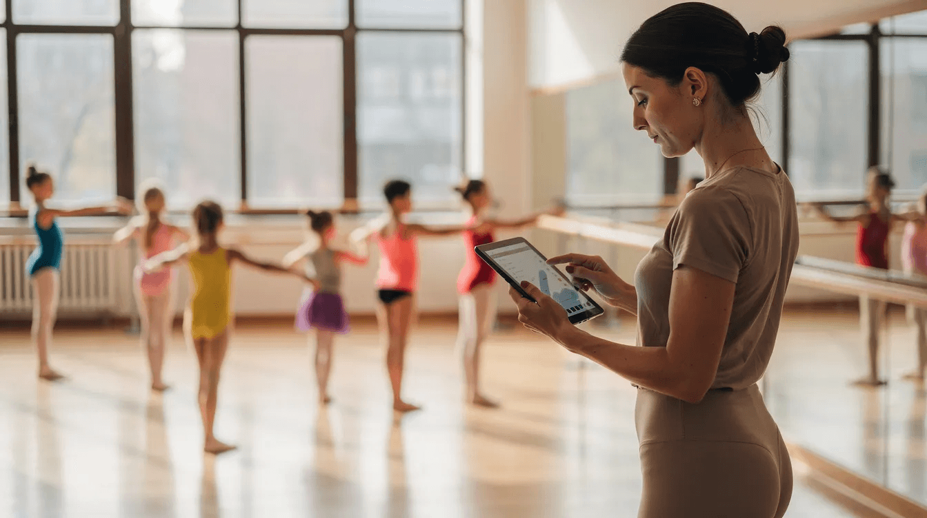 A dance teacher is attentively checking a tablet during class, while young students practice their moves in the background. The scene highlights the use of technology in managing dance lessons, showcasing the integration of productivity tools in a studio environment.