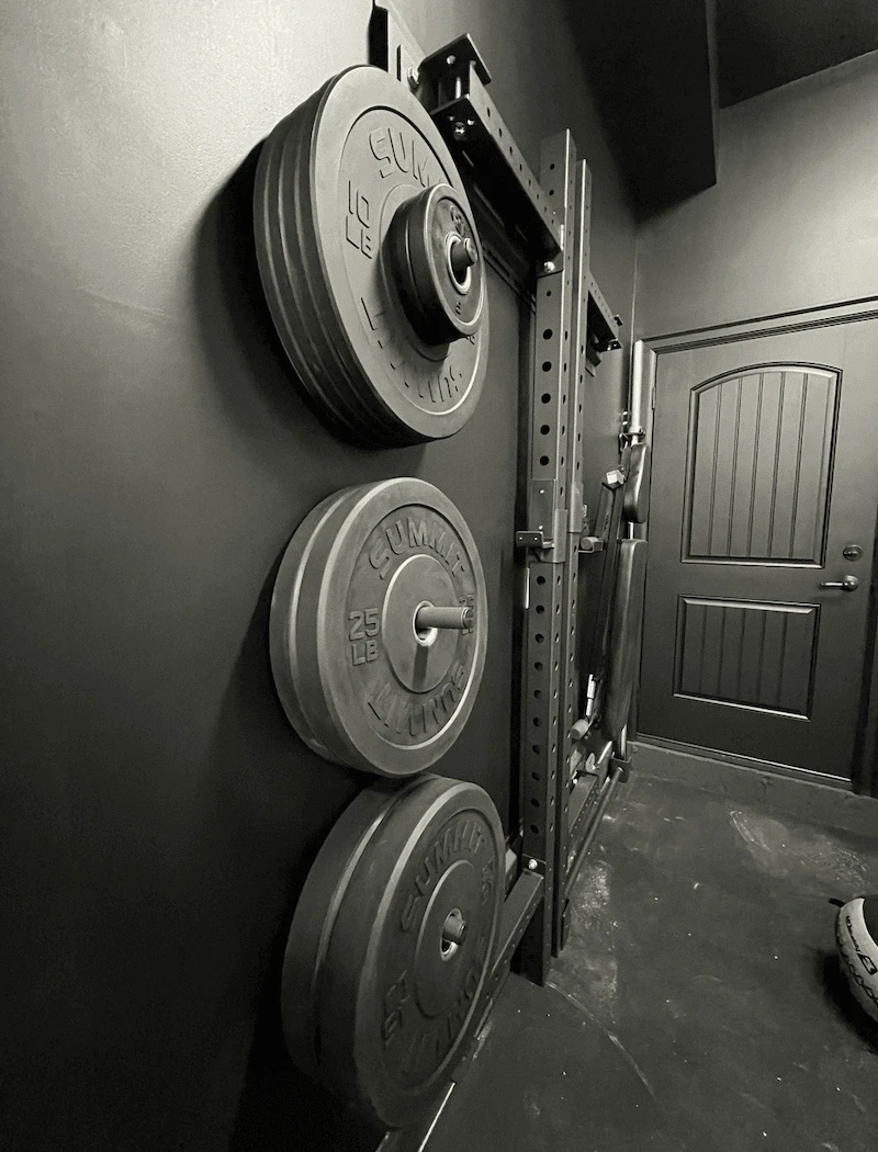 Wall-mounted weight plate storage system beside a power rack in a custom home gym build in Canada.