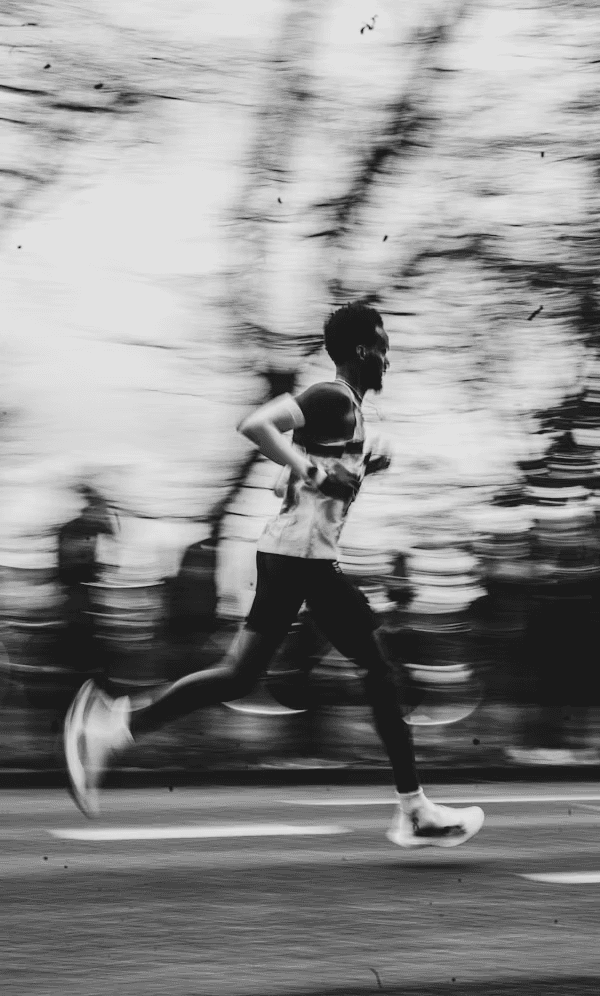 A runner in motion, captured in black and white, with trees blurred in the background.