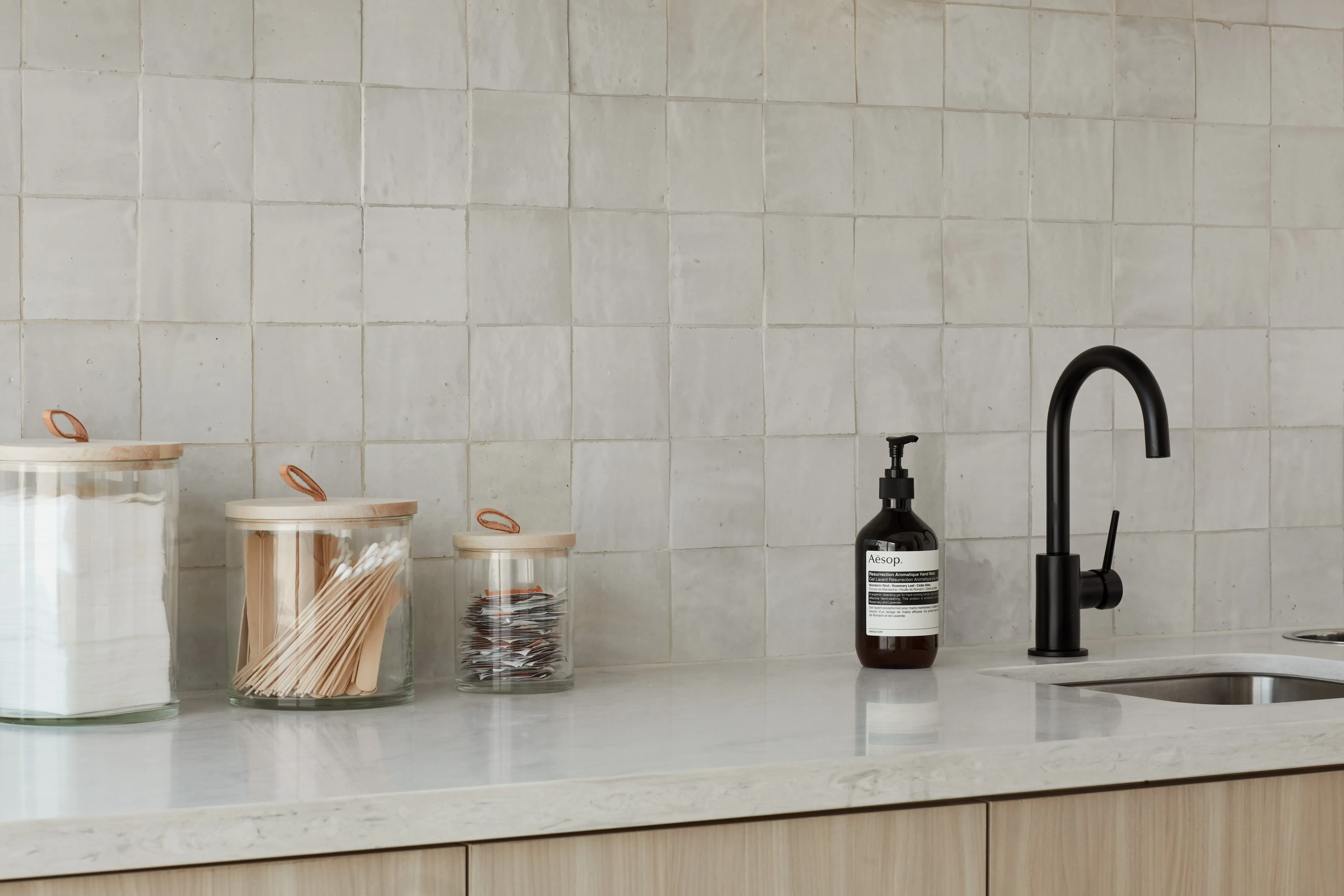 Minimal wellness studio sink area with matte black faucet, handmade tile backsplash, and neutral stone countertop.