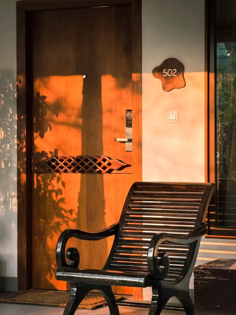 Private patio entrance to a Junior Suite at Vedic Village Kodungallur, wooden armchair and carved door lit by warm evening sunlight