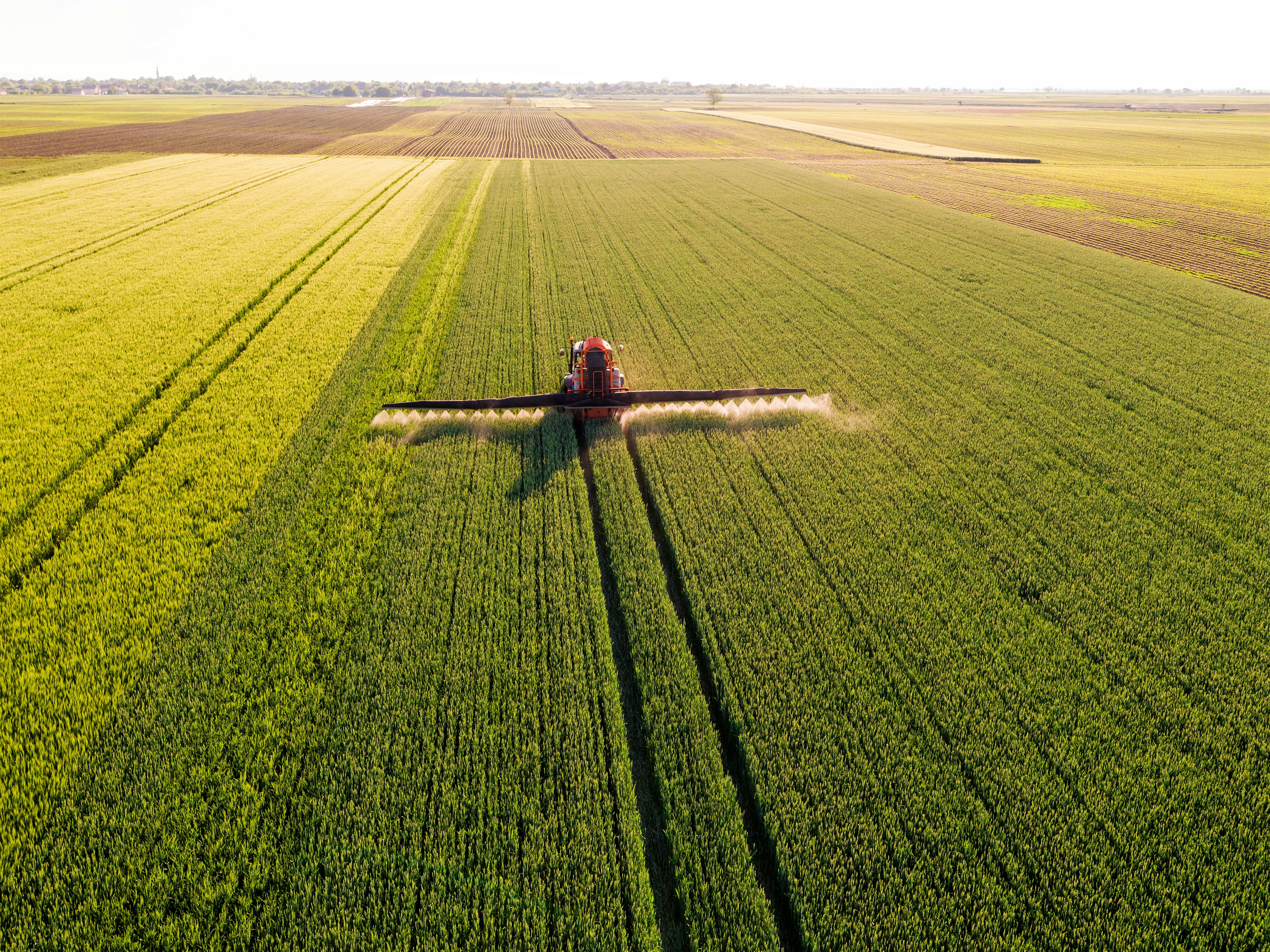 Aerial view of a tractor working in a lush green field during sunset, with long shadows casting across the landscape.