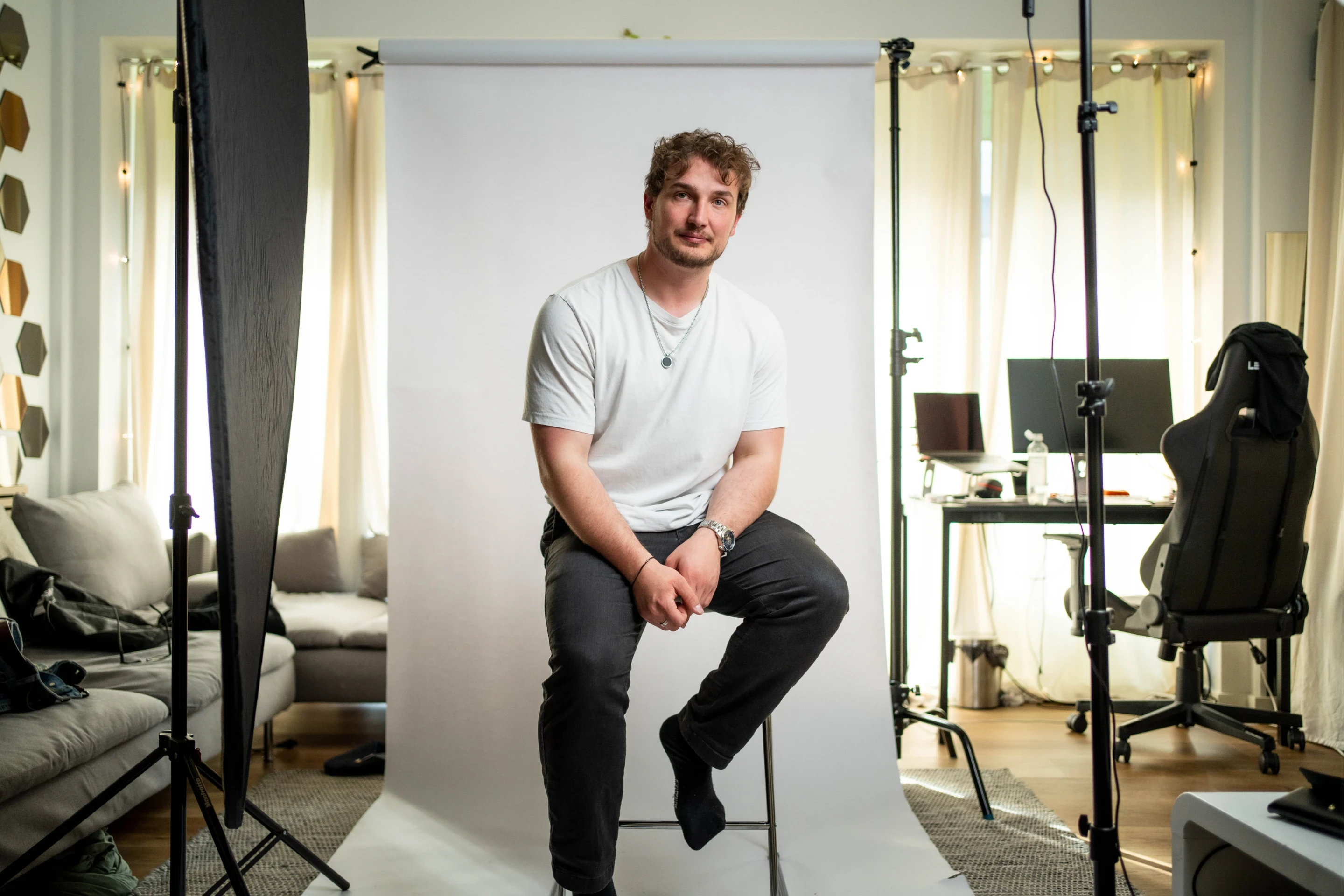 Two people sit at a white table in a dimly lit room, discussing something. The man gestures towards a laptop, while the woman listens attentively.