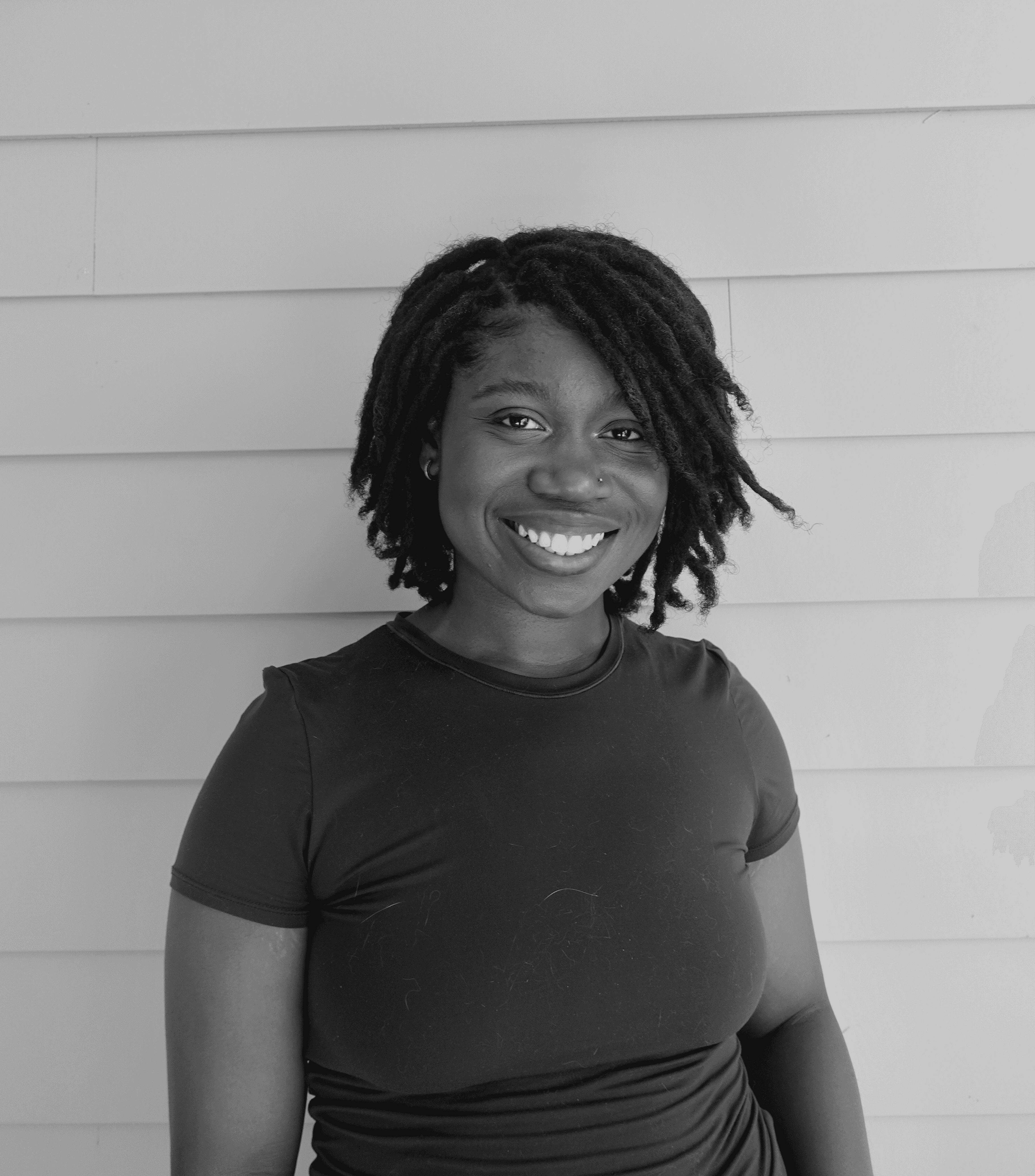 Person wearing a blue puffer jacket and red backpack standing in front of a light blue building on a city street.