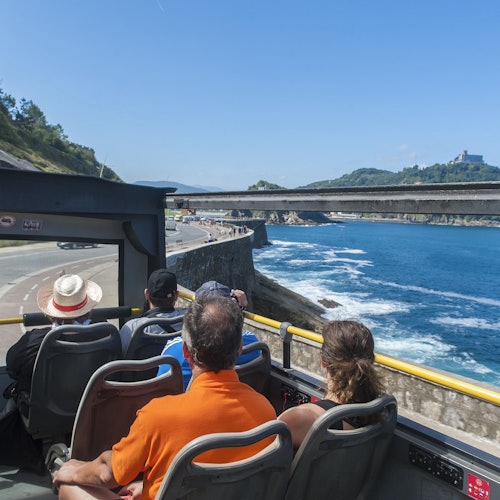 Red double-decker tour bus with "Donostia San Sebastian" signage parked in front of a historic building.
