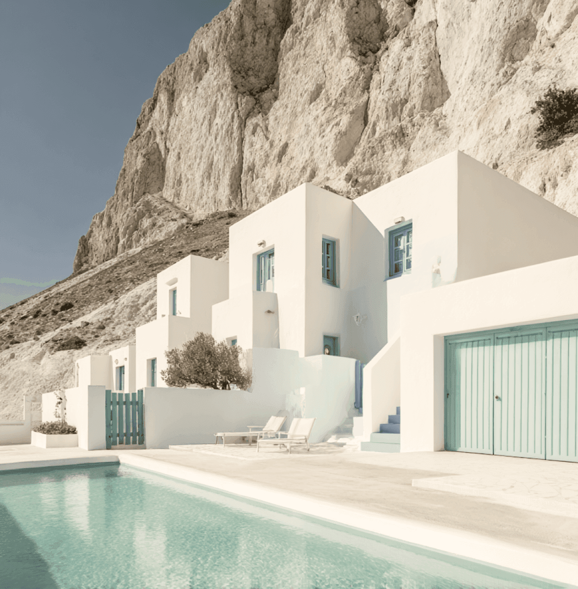 White cliffside villa with turquoise accents and pool under clear blue sky