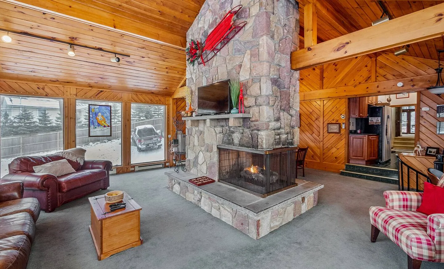 Family room with two-sided stone fireplace, leather sofa and plaid chair at Repeat Retreat