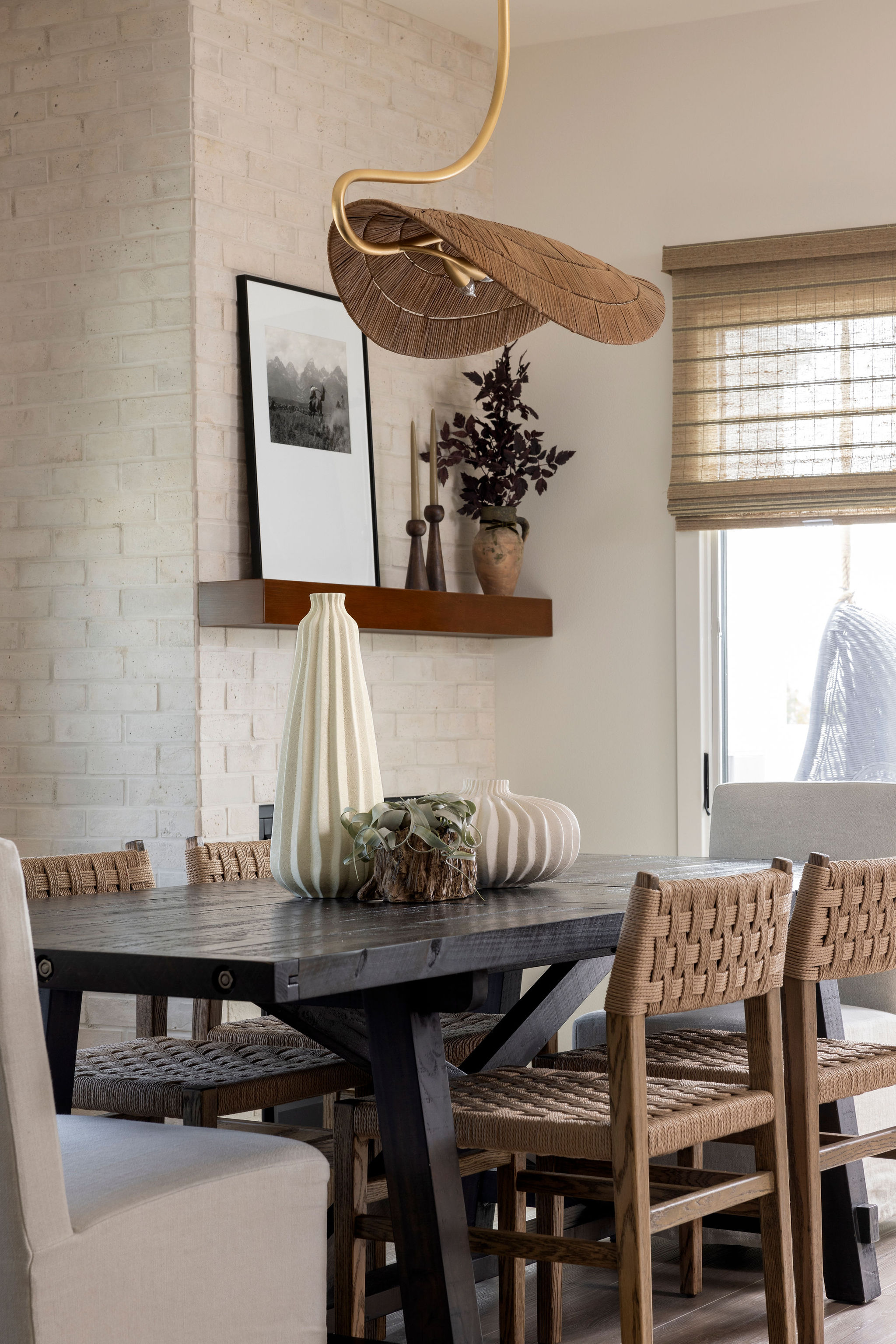 Elegant dining room at featuring a natural wood table, a modern mix of chairs, unique vase centerpiece, and large windows that fill the space with light and charm.