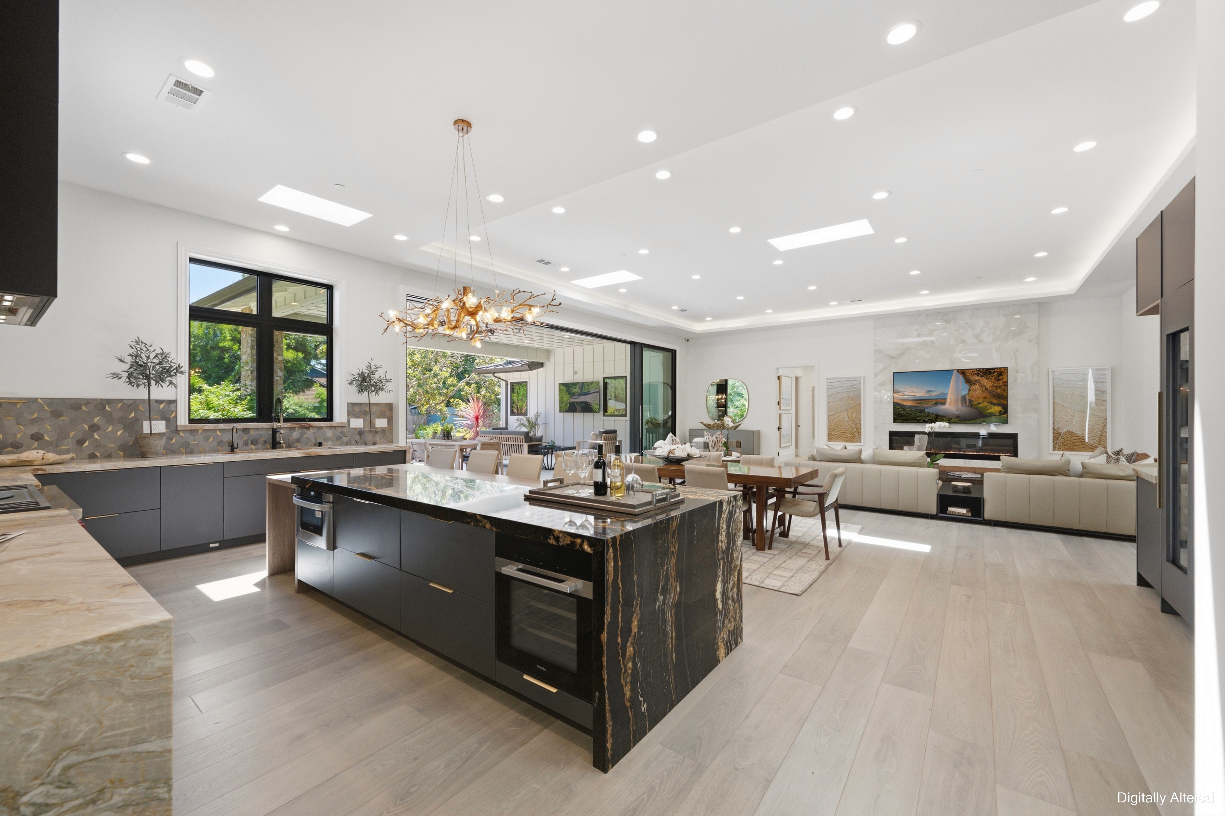 Open kitchen with a dark island, gold chandelier, and dining and living areas beyond.