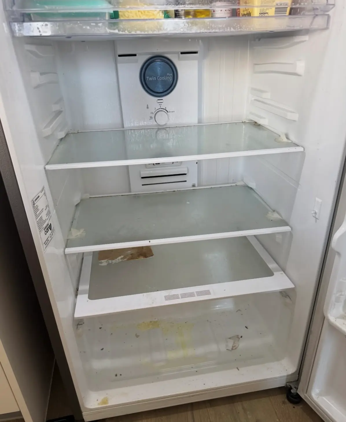 Dirty interior of a refrigerator with food spills and stains on the shelves, before a deep clean.