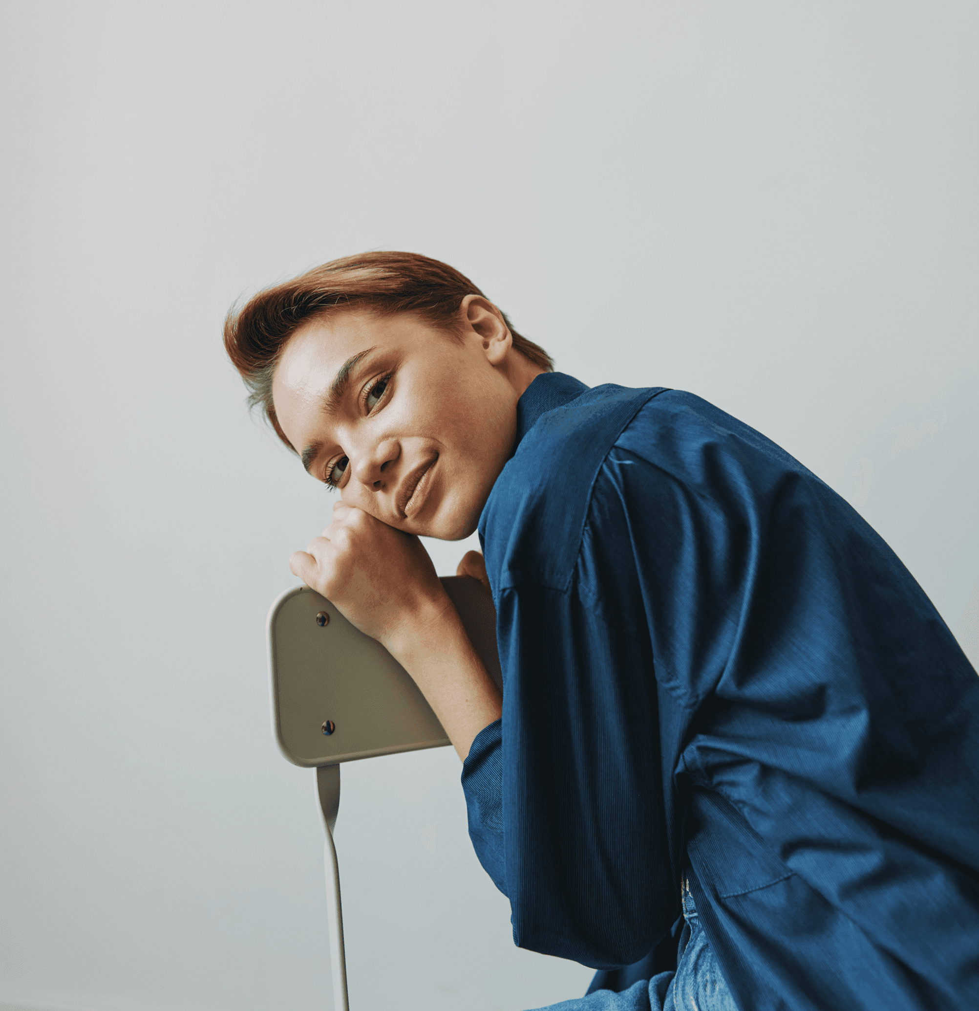 Portrait of young woman leaning on chair in blue shirt, studio shot,.