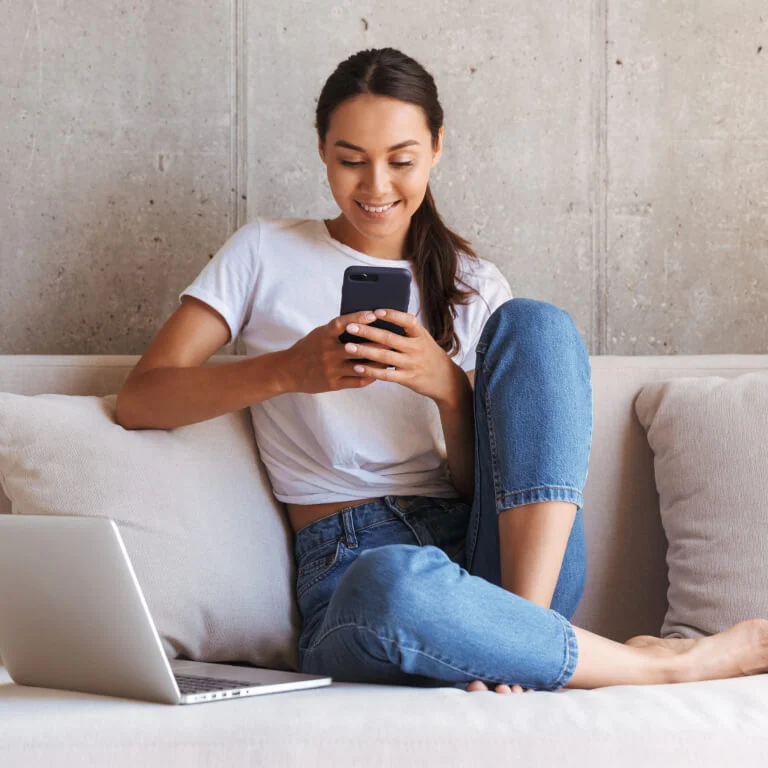 “A person sitting on a couch using the MyPlaceIQ app on their smartphone to control smart air-conditioning and manage room temperatures.