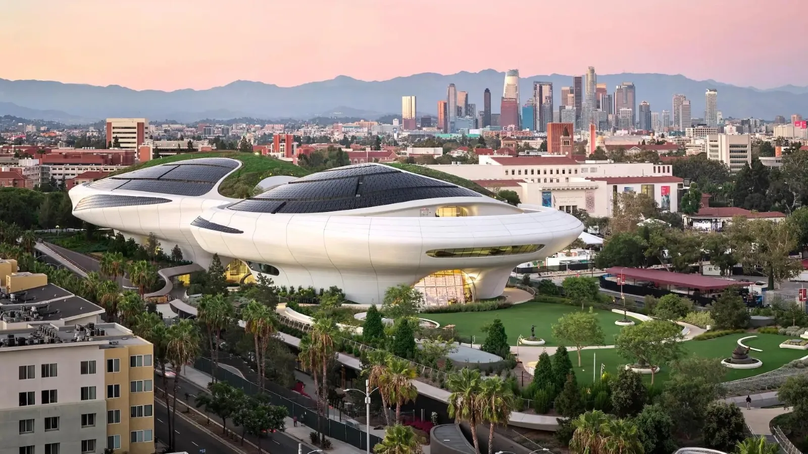 A futuristic museum with sleek, curved architecture and solar panels stands prominently in a lush green park, set against a city skyline at sunset with mountains in the distance.