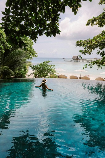 A serene pool surrounded by trees, with a person enjoying the water and a beach visible in the background.