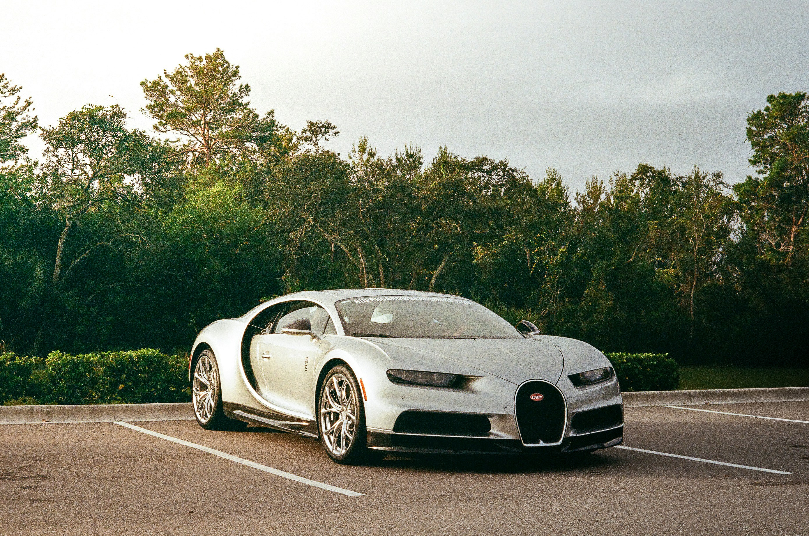 Silver hypercar parked in a lot with trees in the background