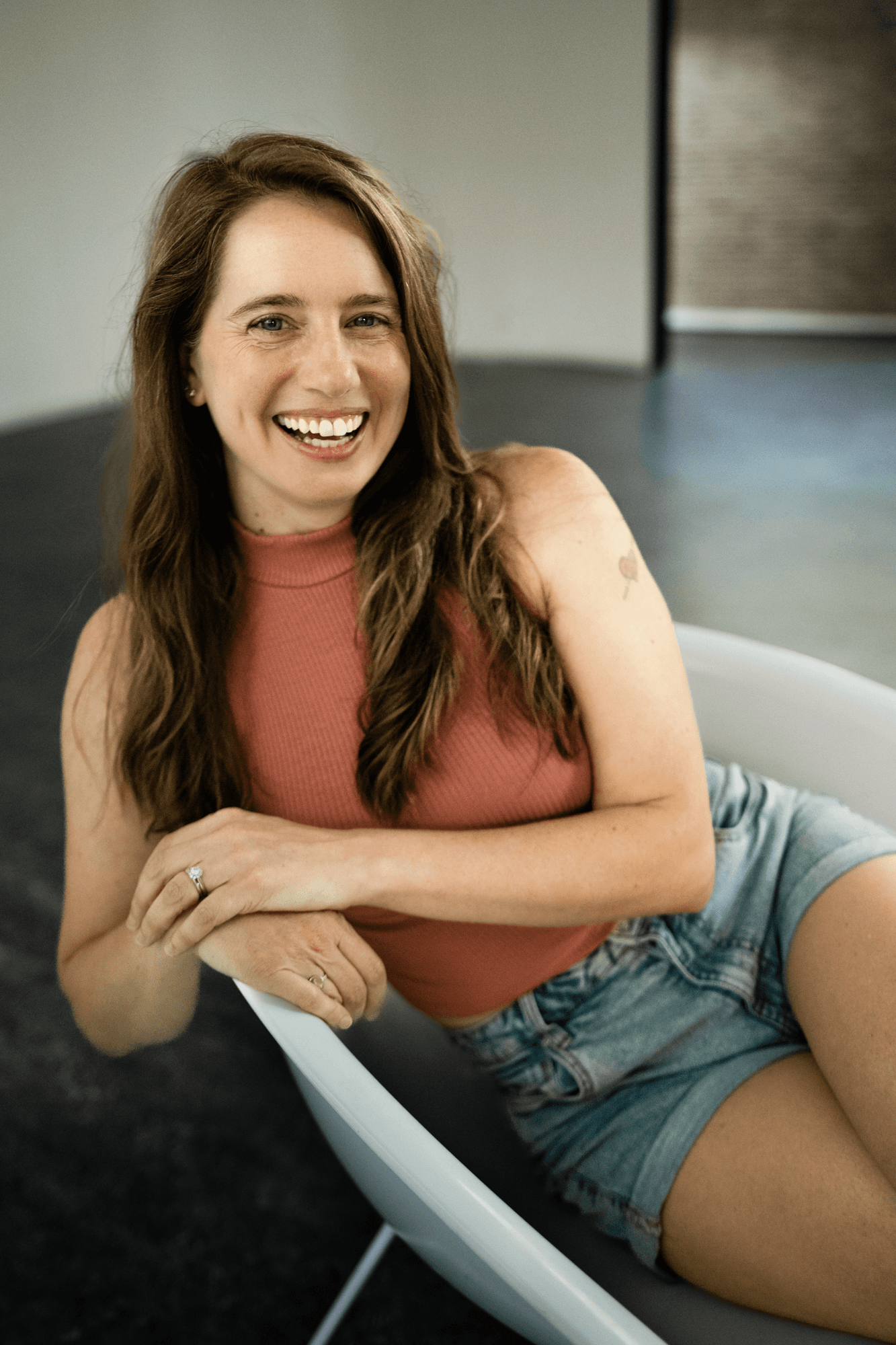 headshot casting photo of Angela Lanier, smiling brown-haired woman in rust top, seated in a modern interior.