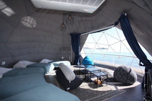 Round glamping tent with multiple beds and a view of the sea