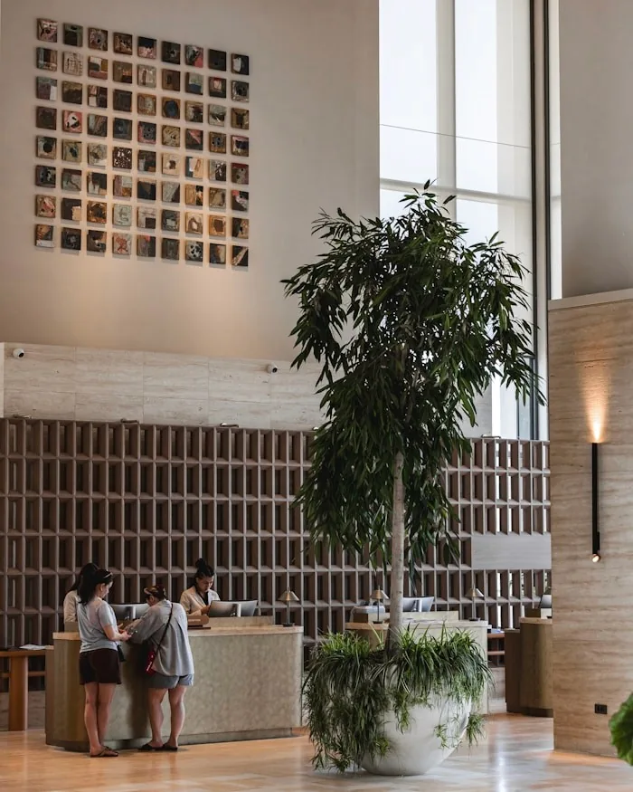 Misafirler, ağaç ve duvar sanatıyla modern otel lobisi resepsiyonu.