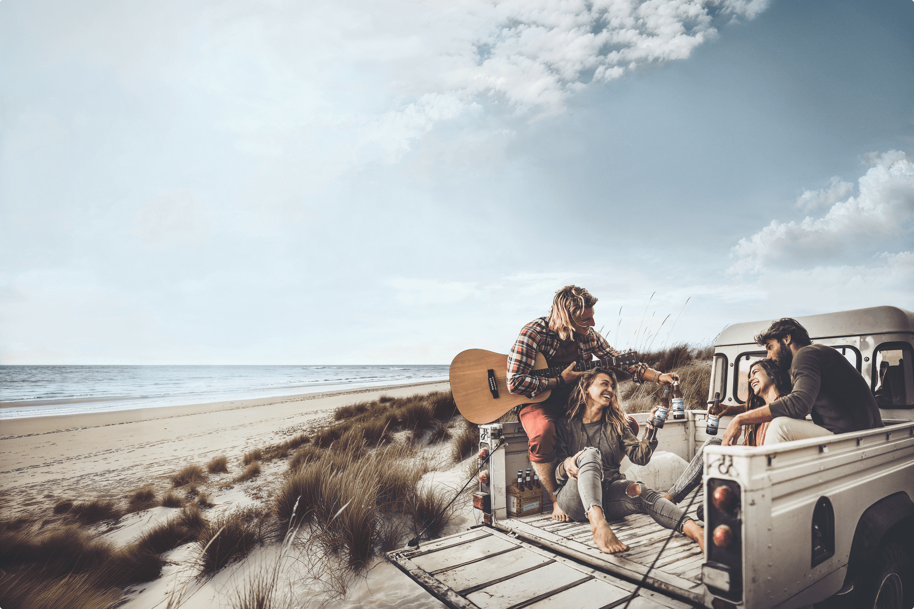 Friends with guitar and beers on a beach picnic.
