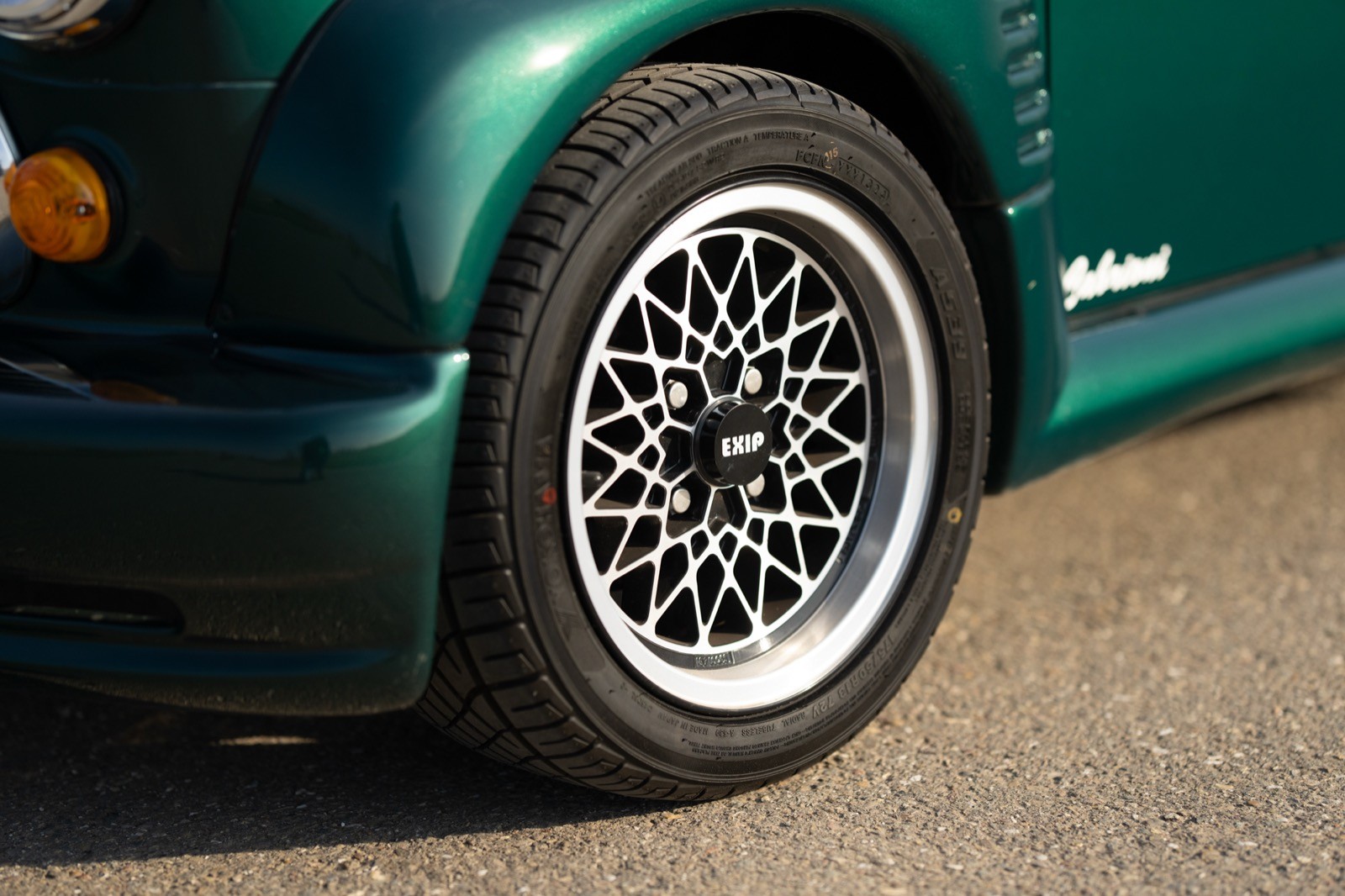 Close-up of a green car's wheel with intricate alloy rim patterns, showcasing a sporty design.