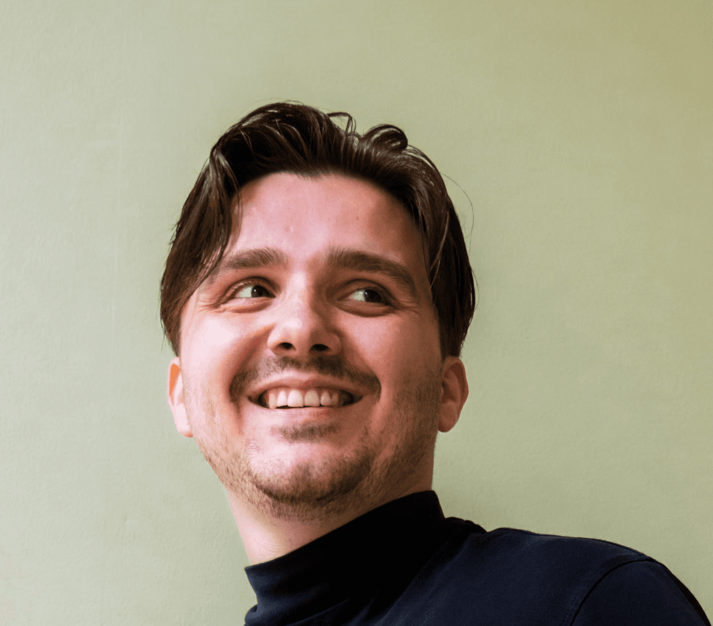 Profilfoto einer lächelnden Person in schwarzer Kleidung vor einem grünen Hintergrund