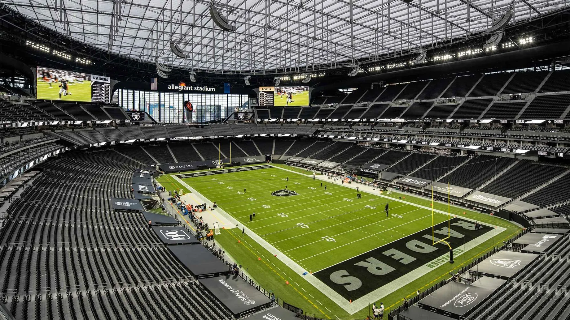 Interior of Allegiant Stadium featuring the Raiders-branded football field under a transparent domed roof, with empty black seating and massive digital screens. Highlights the venue’s state-of-the-art facilities for NFL games and events.