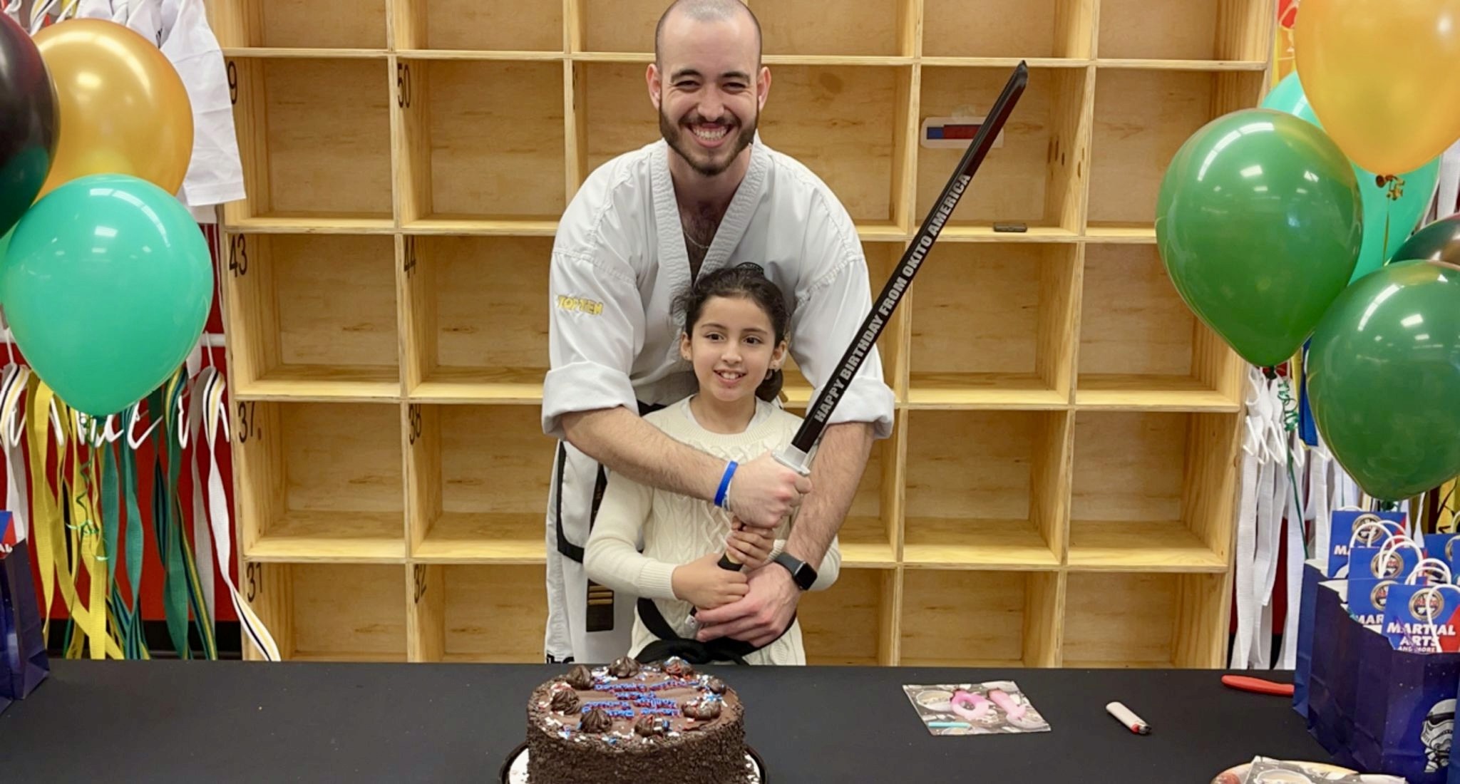 Smiling child and team holding a sword about to cut a cake.