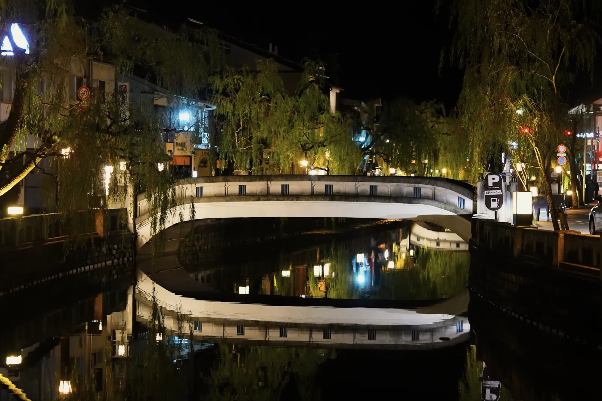 A stone bridge over the Kinosaki canal lit at night with inn windows reflected in the water.