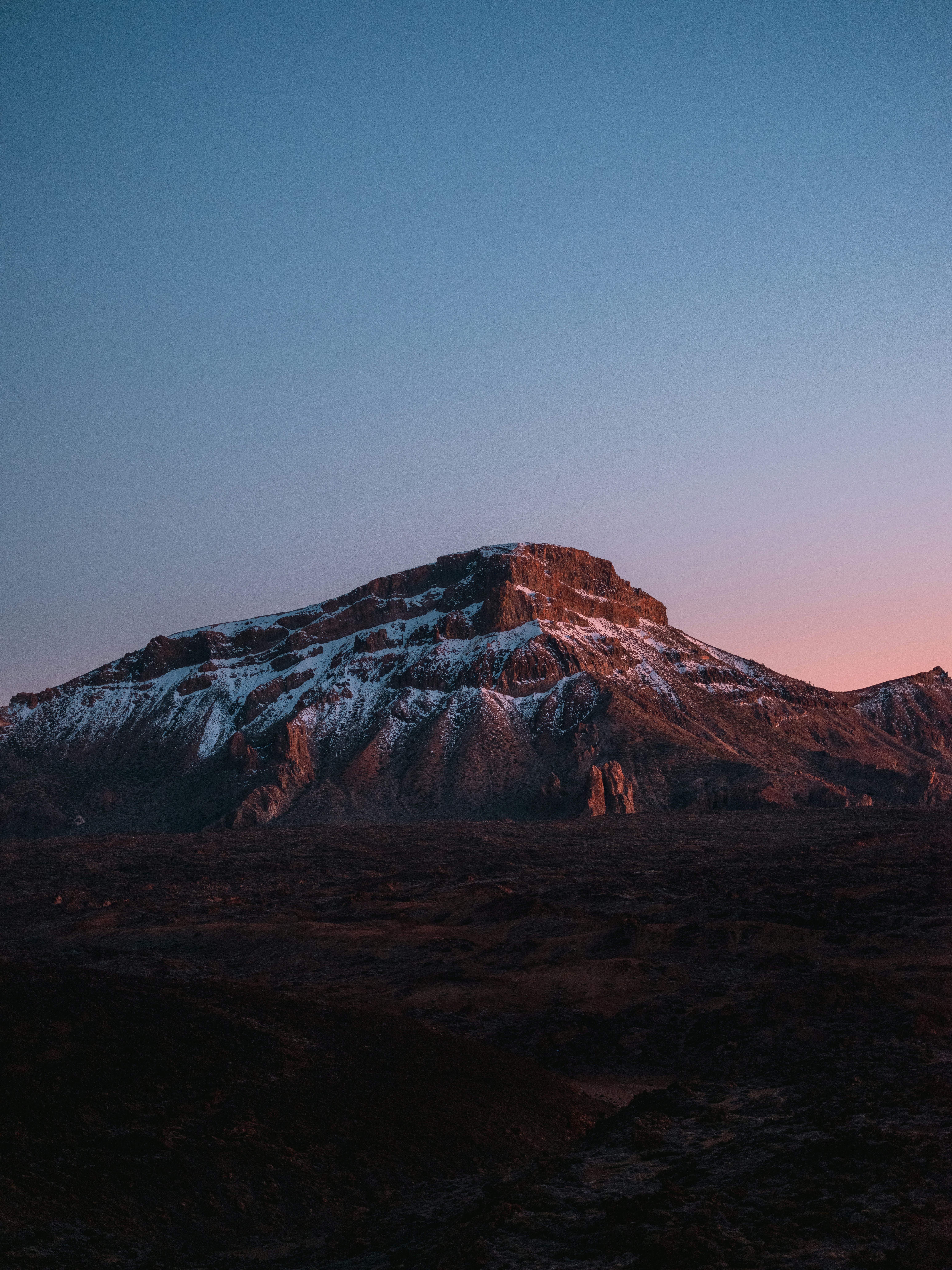 Snow-capped mountain peak at sunrise with rocky foreground