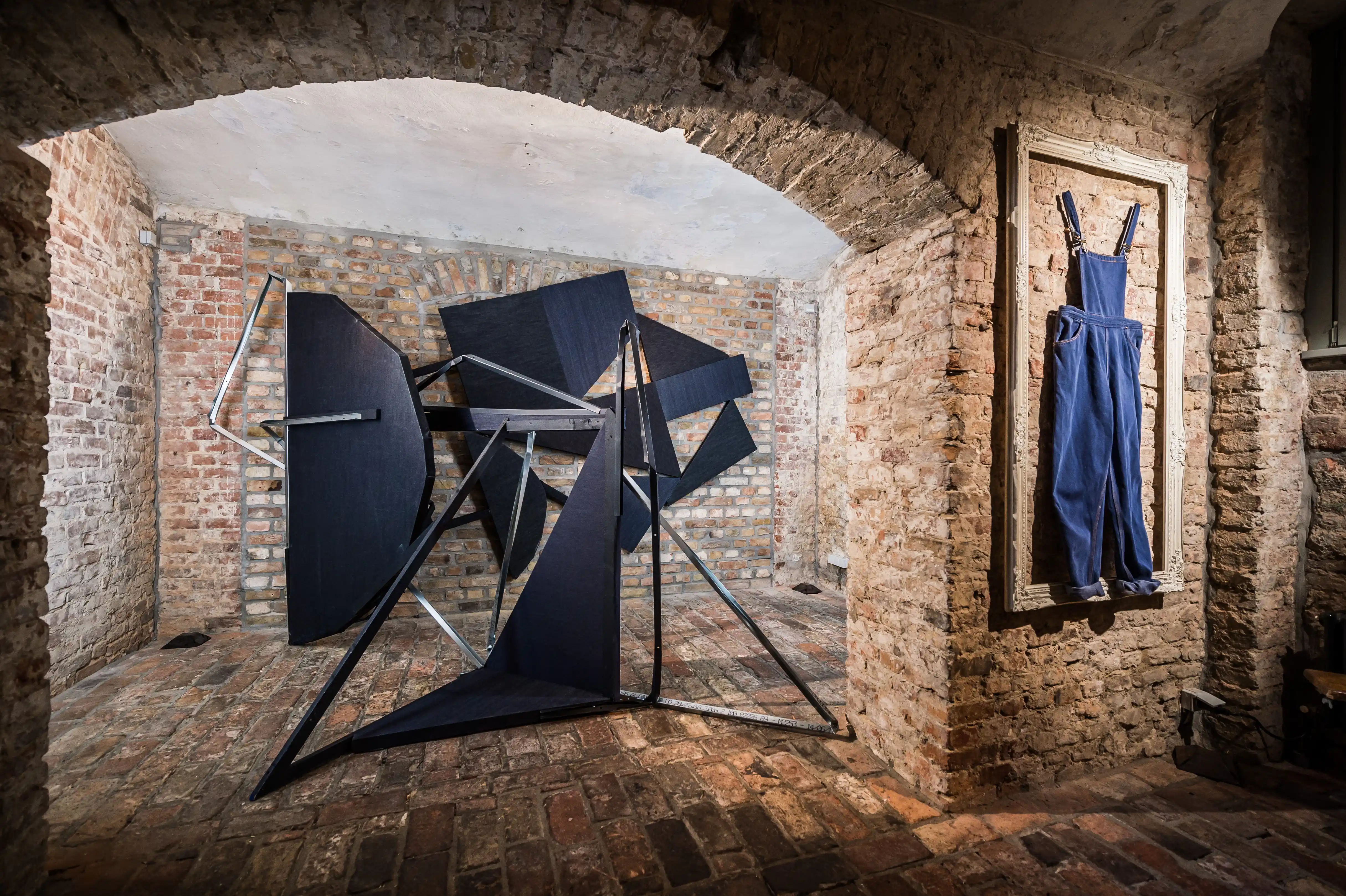 Brick vault at the MUSTANG Street ART Lab with a black geometric metal sculpture and blue denim dungarees framed on the wall.