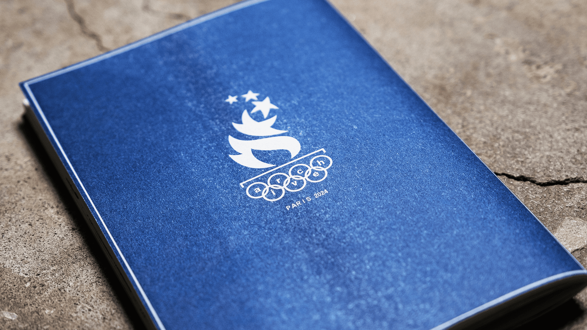 Archive PDF wide open Paris 2024 navy blue zine cover featuring the Paris Olympics flame and stars emblem with archive pdf lettering integrated into the rings on a stone surface