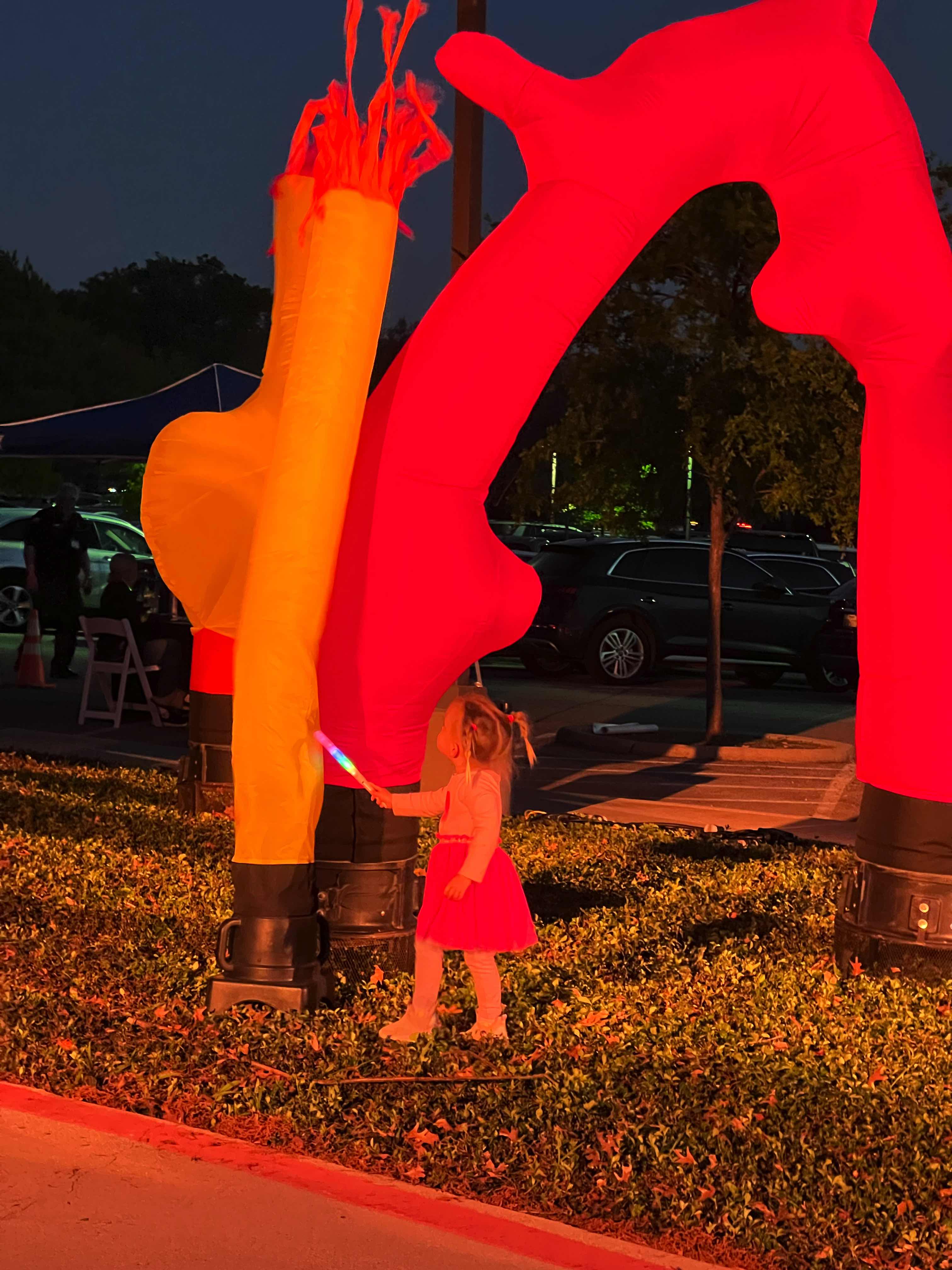 A child in a pink outfit stands next to a large colorful sculpture under a night sky.