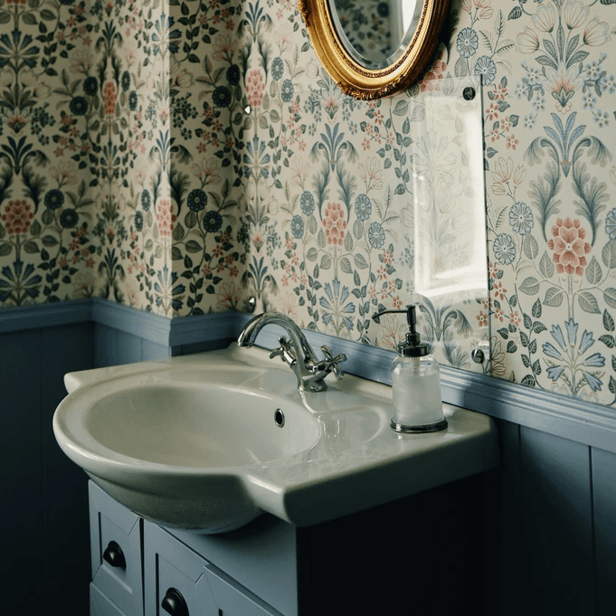 A bathroom with floral wallpaper and gold mirror.
