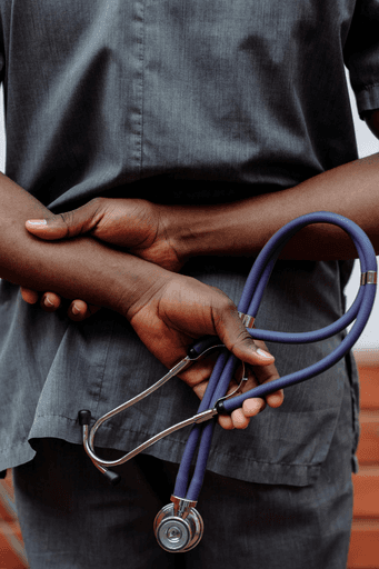 A person in scrubs holds a stethoscope with one hand while resting the other hand on their arm.