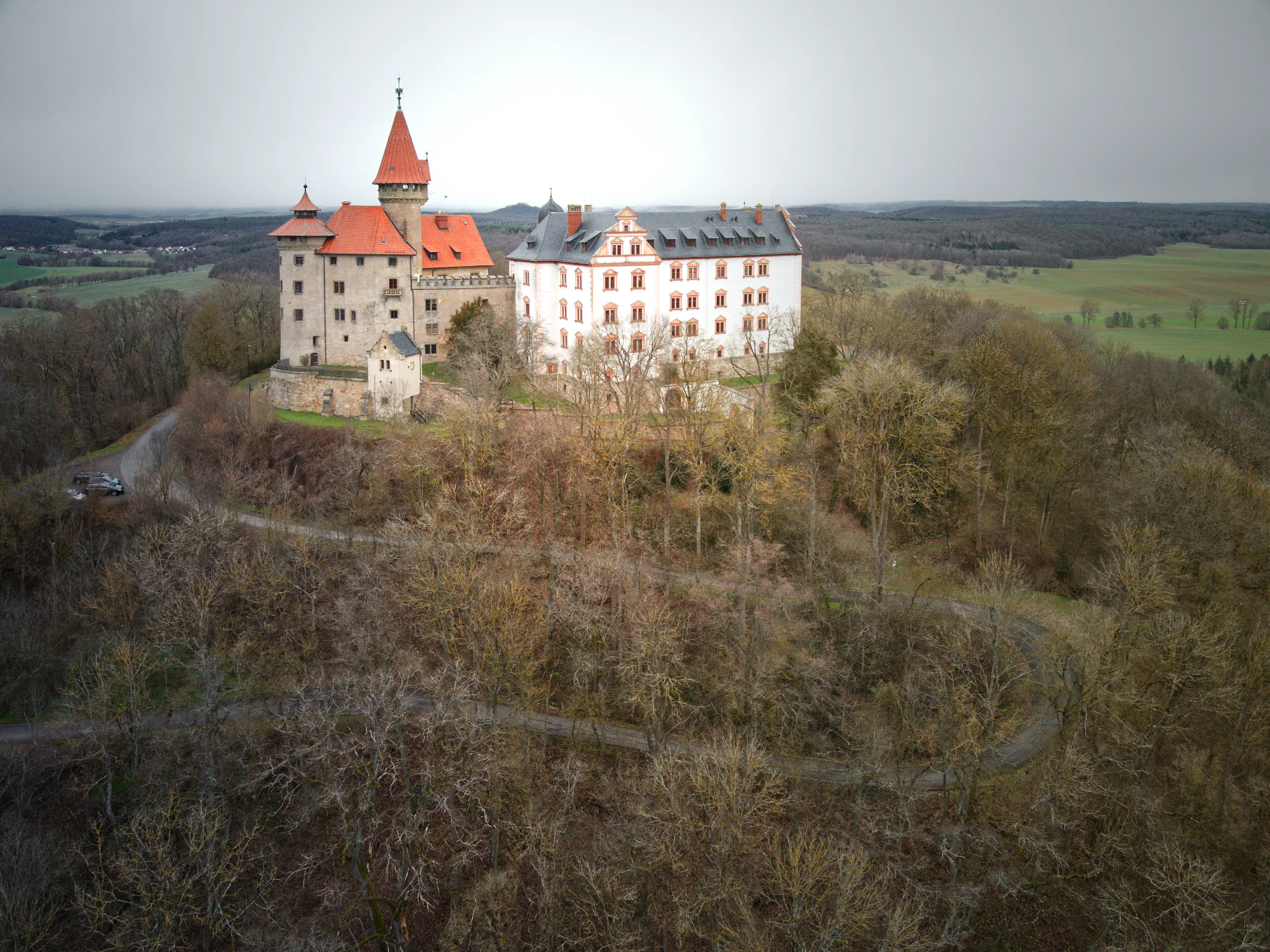 Luftaufnahme der Veste Heldburg mit dem Deutschen Burgenmuseum auf einem bewaldeten Höhenzug in Thüringen.