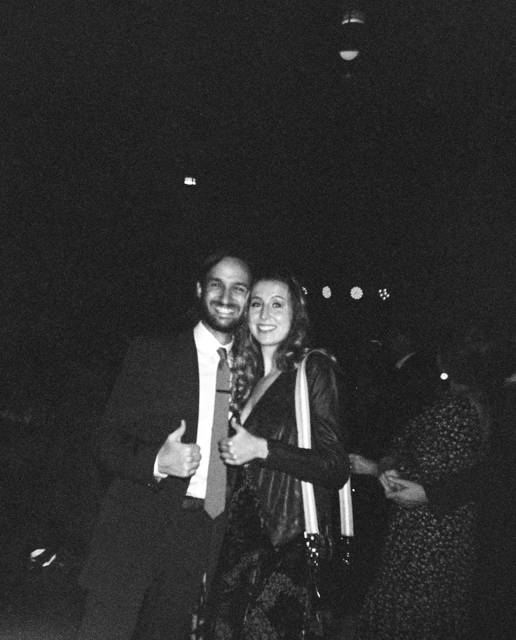 A man in a tux and a girl in a jacket both are smiling and have a thumbs up 