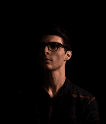 a man with glasses standing in the dark
