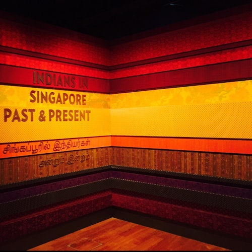 A museum exhibit corner with colorful patterned walls and the text "Indians in Singapore: Past & Present" in English and Tamil.
