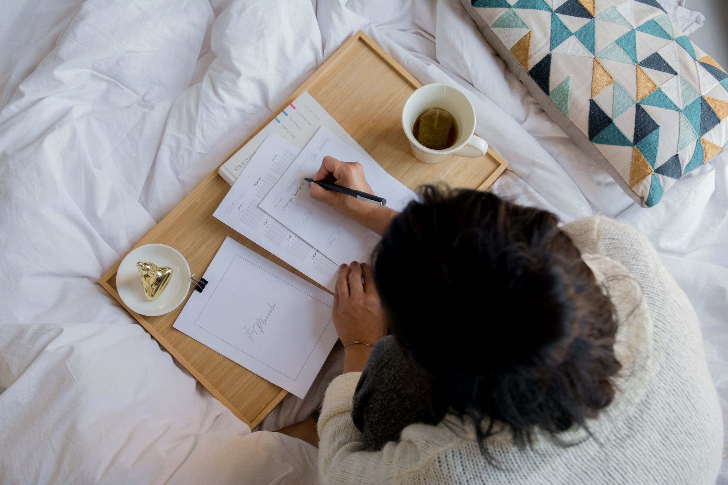 A person journaling on a bed beside a cup of tea