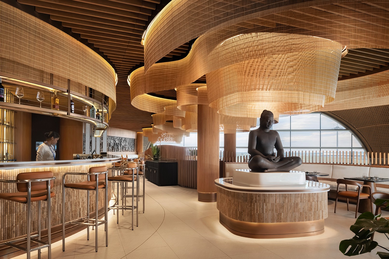 Interior detail of Malis Restaurant featuring a central Buddha statue and flowing mesh gold lighting fixtures balancing traditional Cambodian cultural elements with world-class contemporary design aesthetics