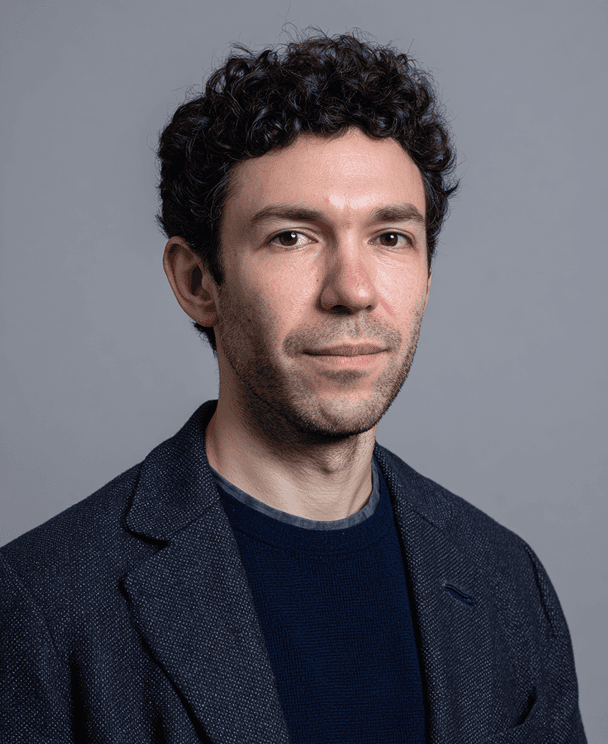 A man with curly hair dressed in a blue shirt poses for the photo.