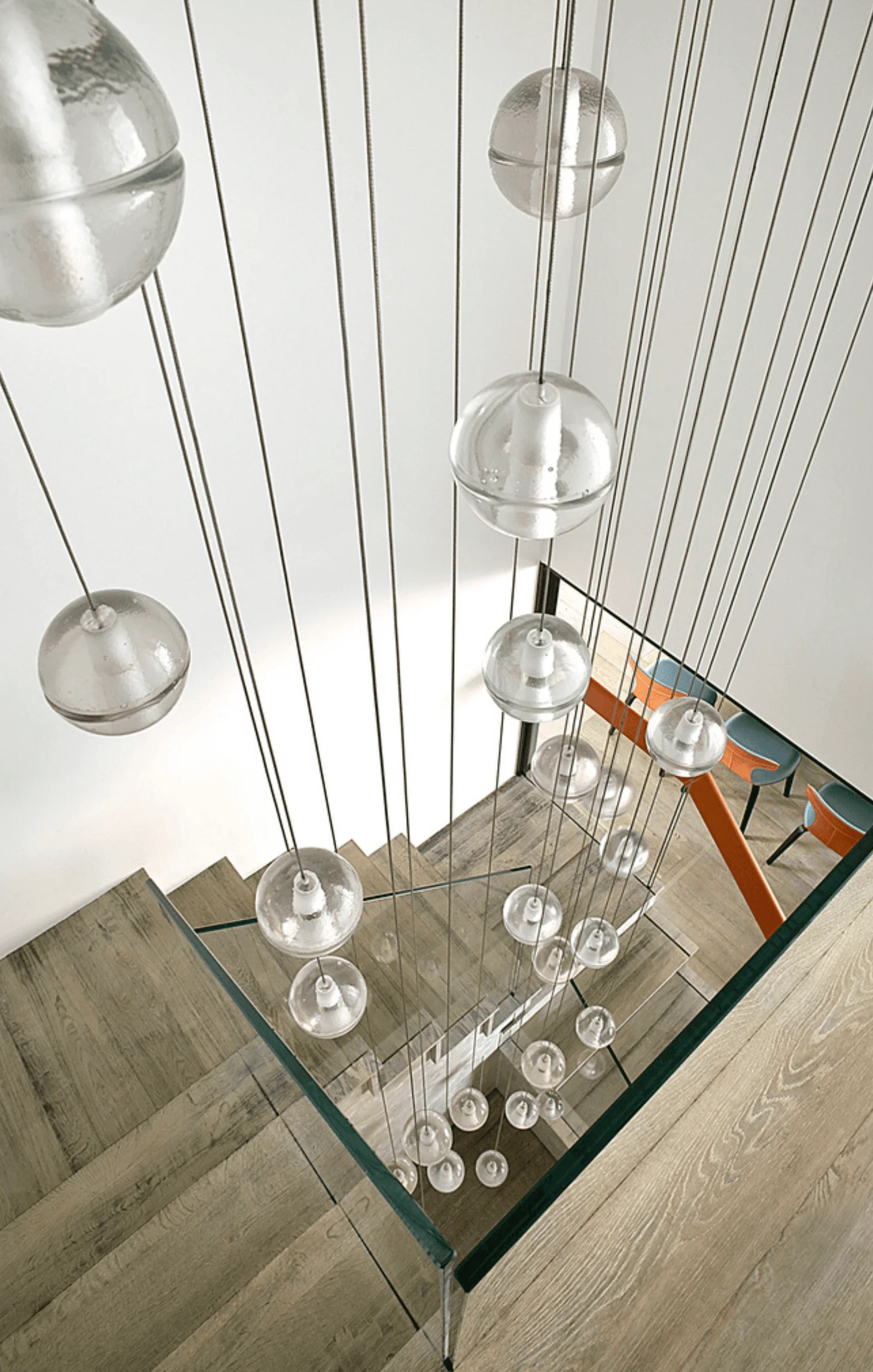 A view looking down the stairwell through a cascade of glass globe pendant lights toward the dining area