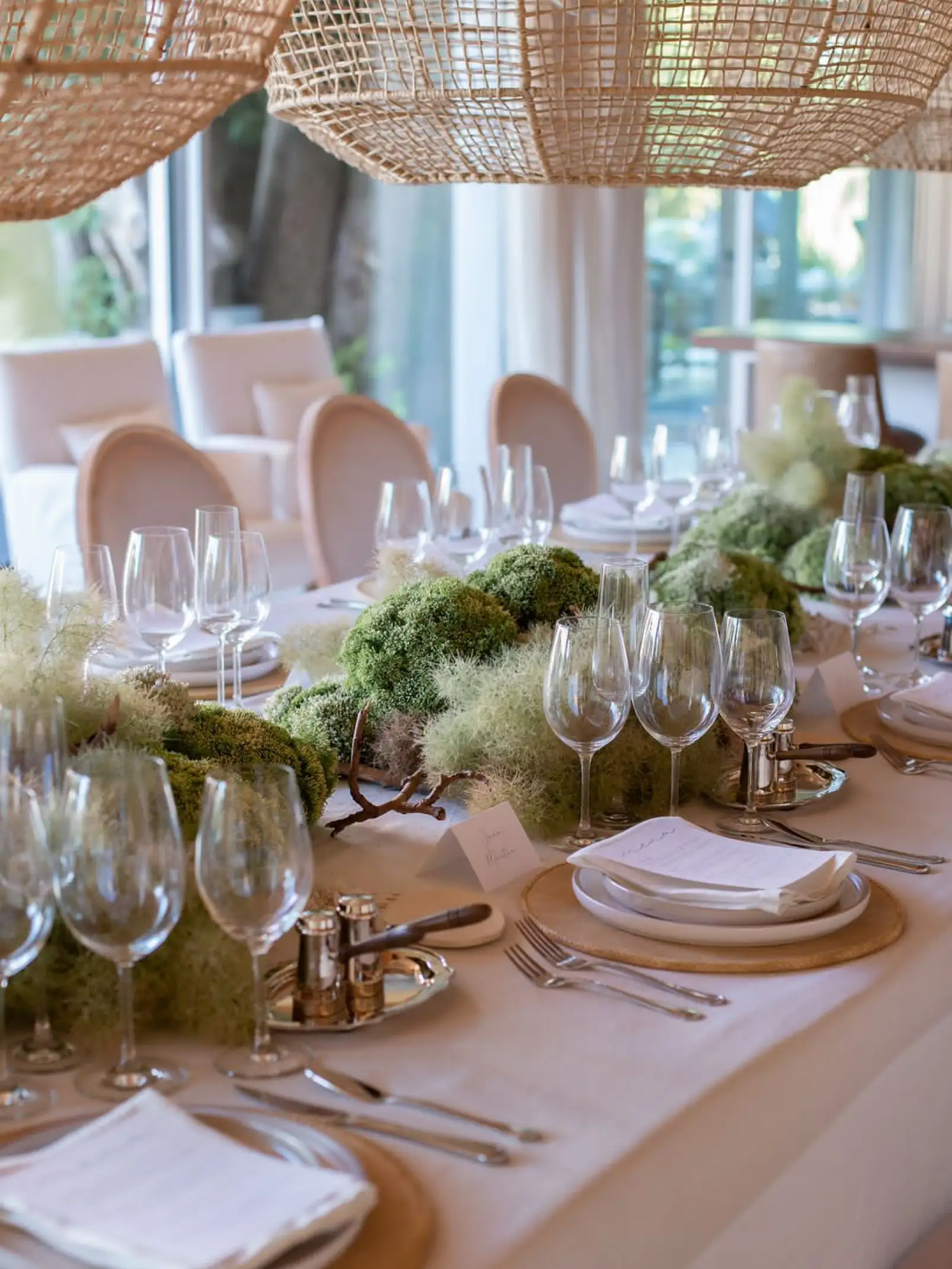 Detalle de mesa elegante con copas de vino y champaña, cubiertos de plata y decoración natural de musgo
