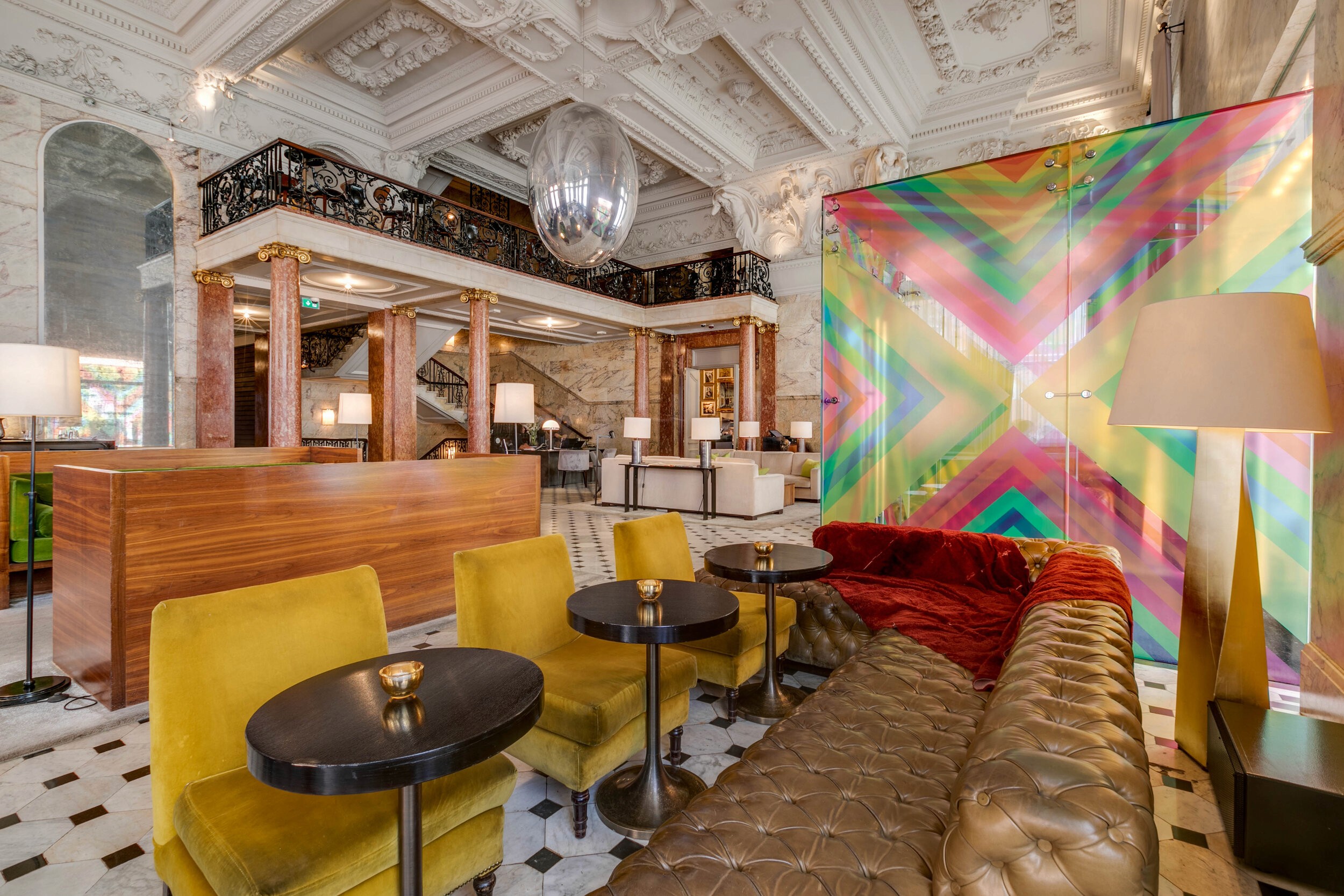 A lounge area with yellow and leather seating, a colorful translucent panel, and a luxurious marble interior.