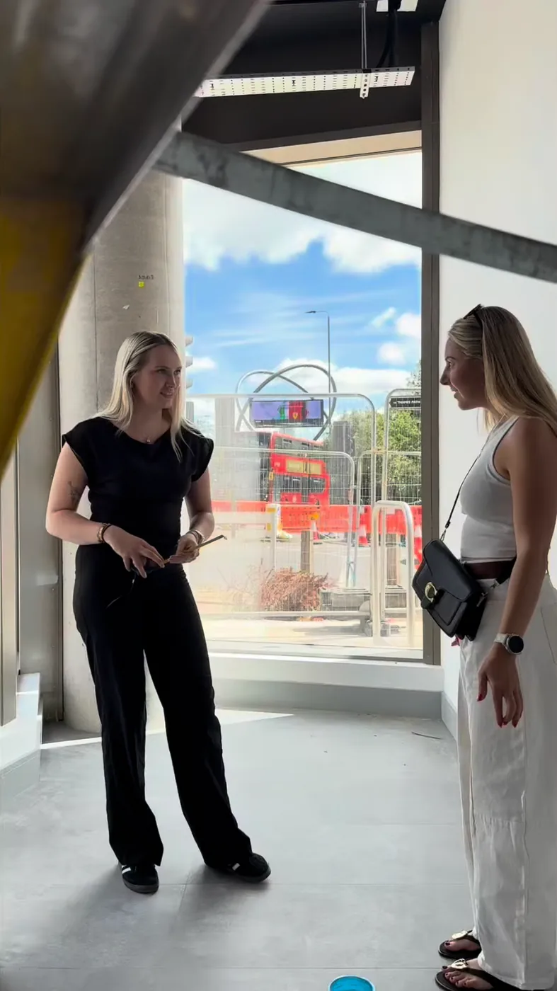 Two women talking in a bright, empty room with large windows